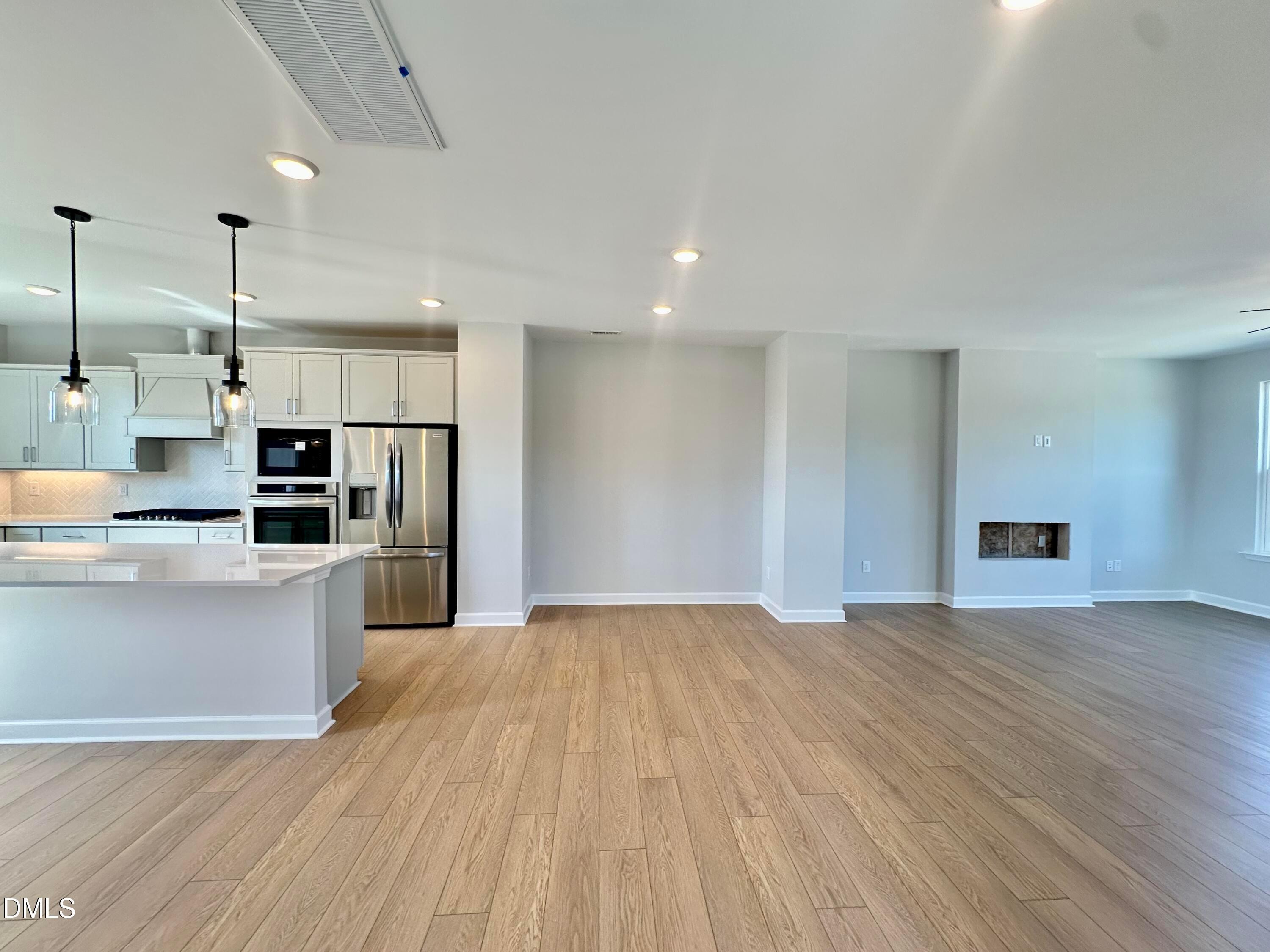 Modern open-concept kitchen with white cabinets, stainless appliances, quartz island, and living area fireplace in Davidson Homes The Avery, Knightdale NC