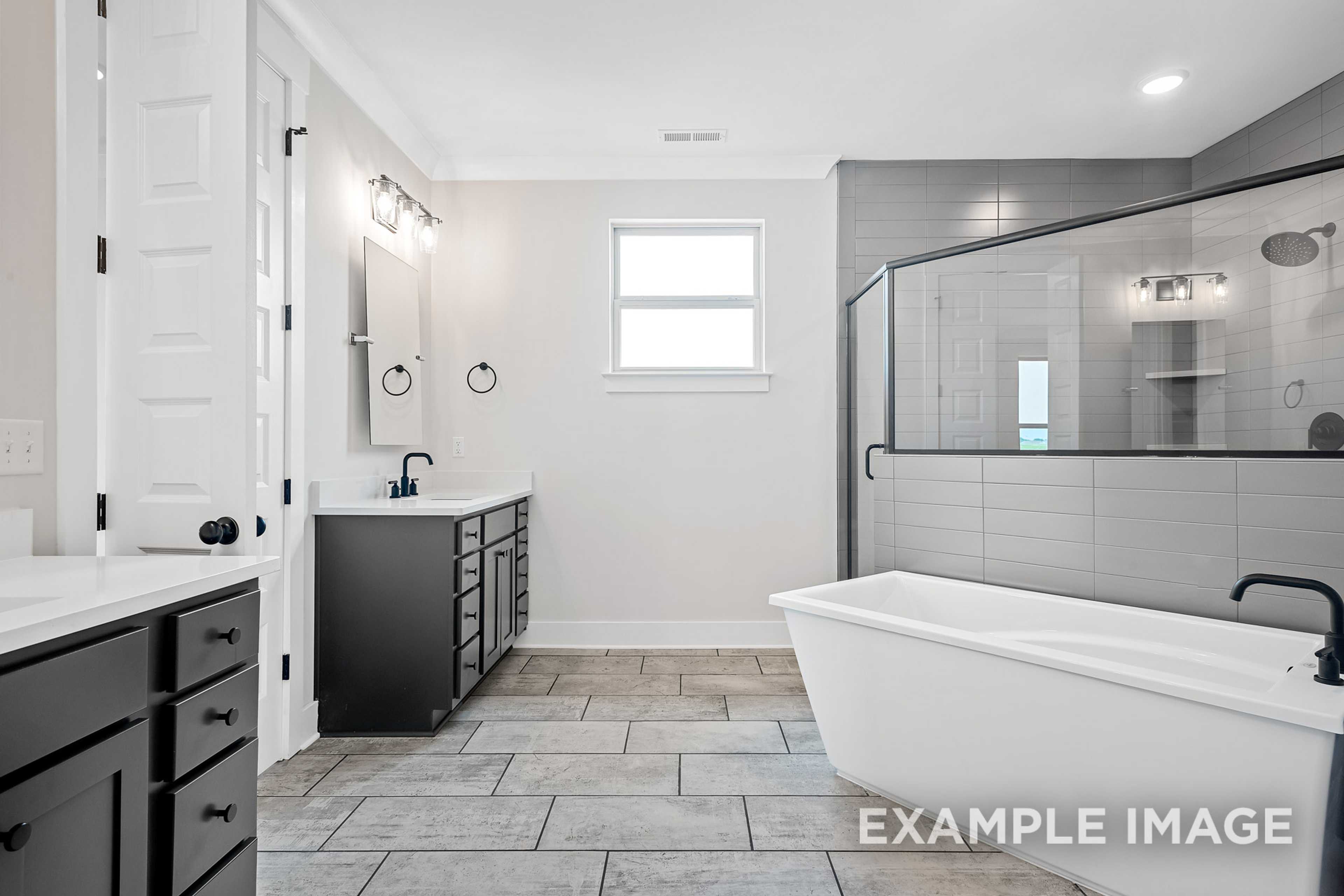 Spacious master bathroom in The Hawkins with dual black vanities, freestanding tub, and frameless glass shower