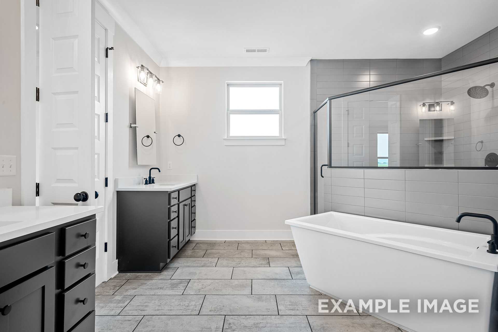 Spacious master bathroom in The Hawkins with dual black vanities, freestanding tub, and frameless glass shower