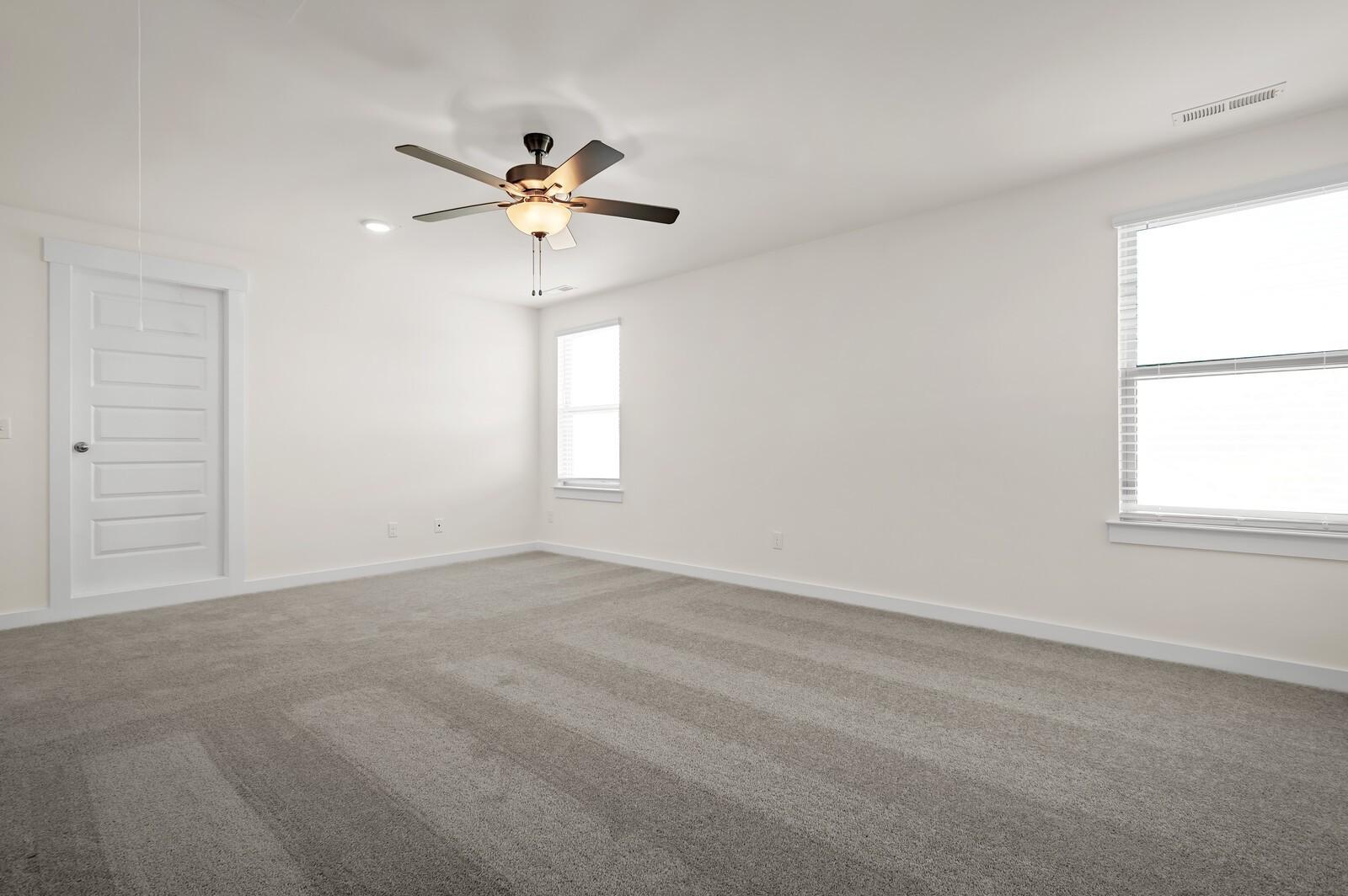 Spacious, carpeted bedroom with ceiling fan in The Ash A floor plan at Woods Crossing in Gallatin, Tennessee.