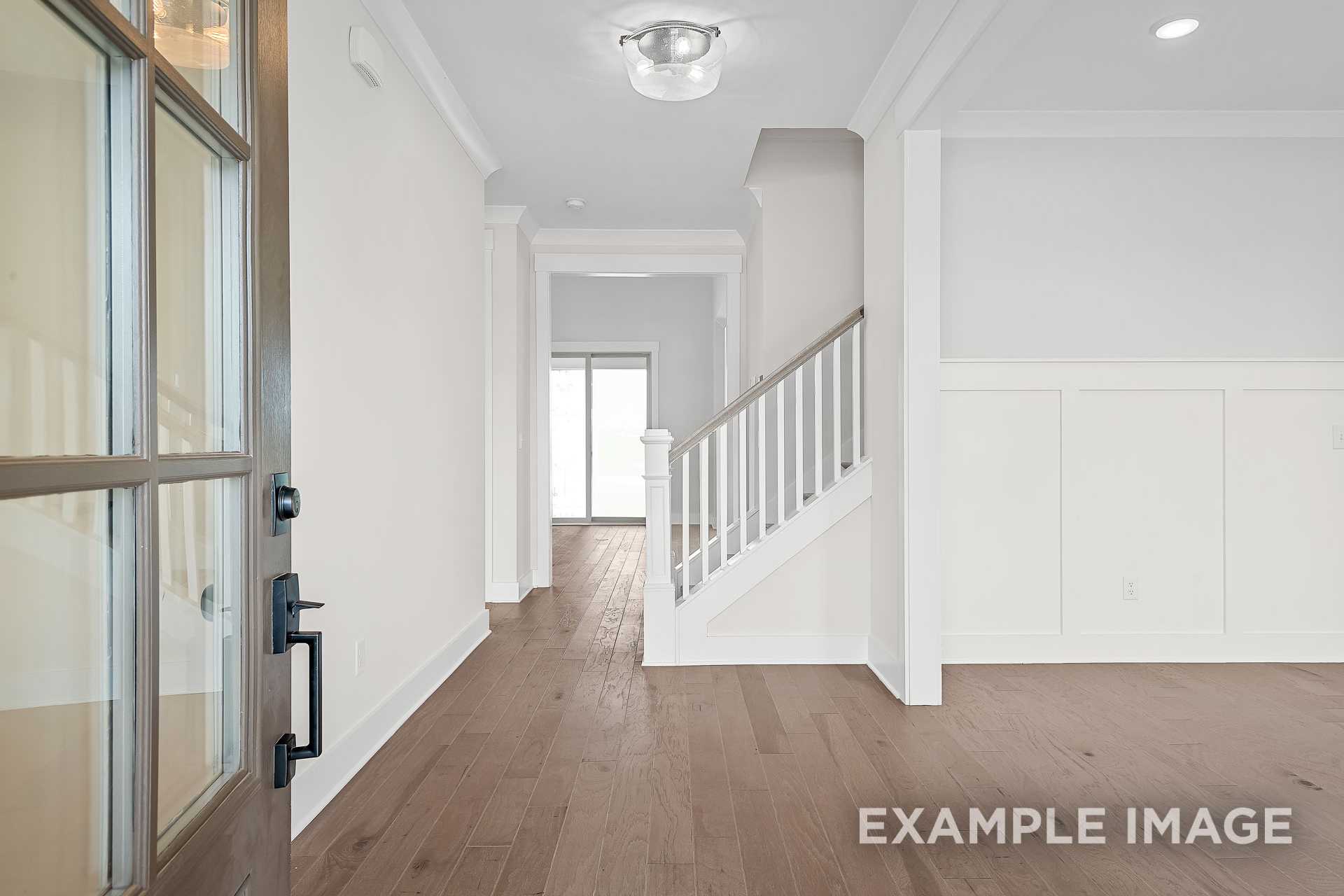 Spacious entryway of The Hawkins 2-story home with glass-paneled front door, hardwood floors, and white staircase