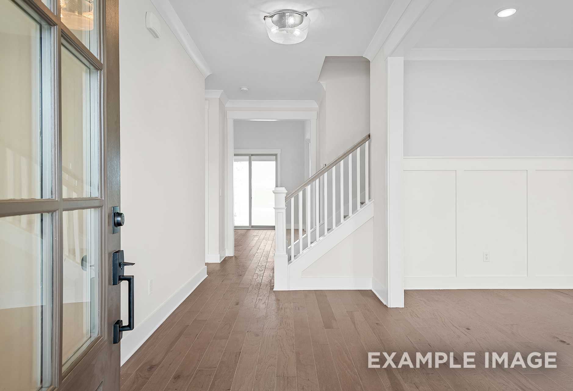 Spacious entryway of The Hawkins 2-story home with glass-paneled front door, hardwood floors, and white staircase