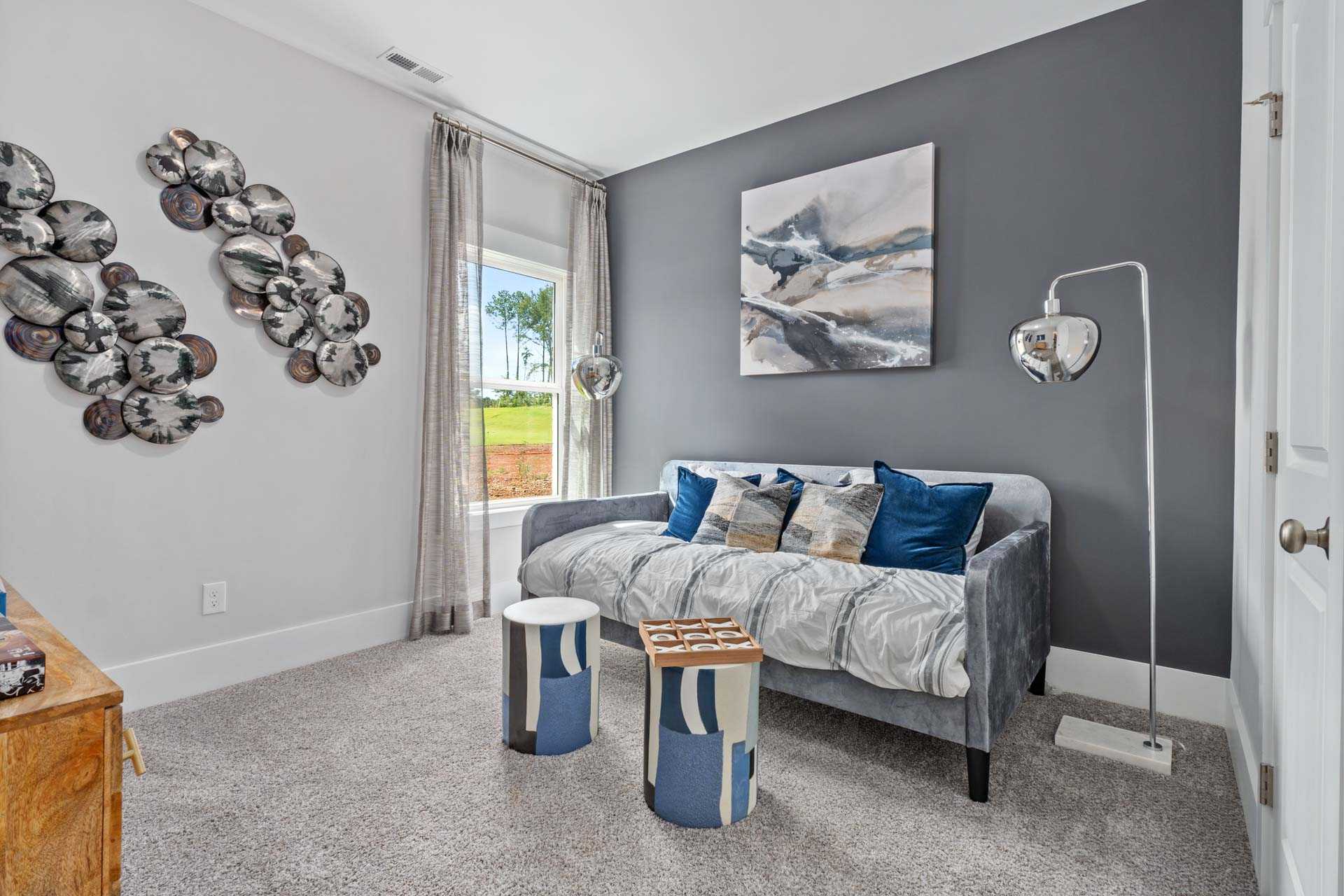 Cozy den with gray loveseat, blue pillows, abstract art and window view at Blue Spring in Huntsville Alabama