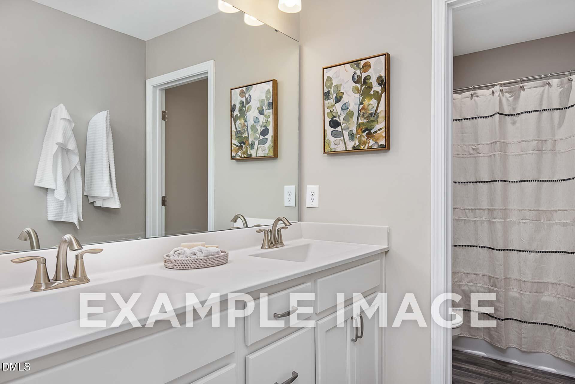 Modern double vanity bathroom with gray walls, white sinks, and eucalyptus art in Davidson Homes The Ash B, Lillington, NC