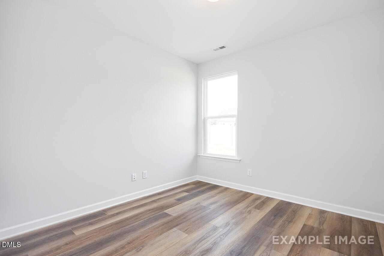 Bright empty bedroom featuring white walls, large window, and wood-look laminate flooring in The Daphne C, Davidson Homes, Zebulon, NC