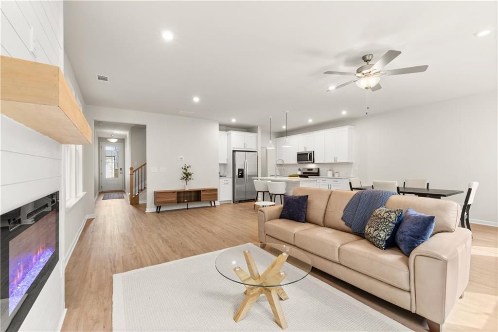 Open-concept living room with electric fireplace, beige sofa, glass coffee table, and white kitchen island in Davidson Homes The Marion B, Kennesaw, GA