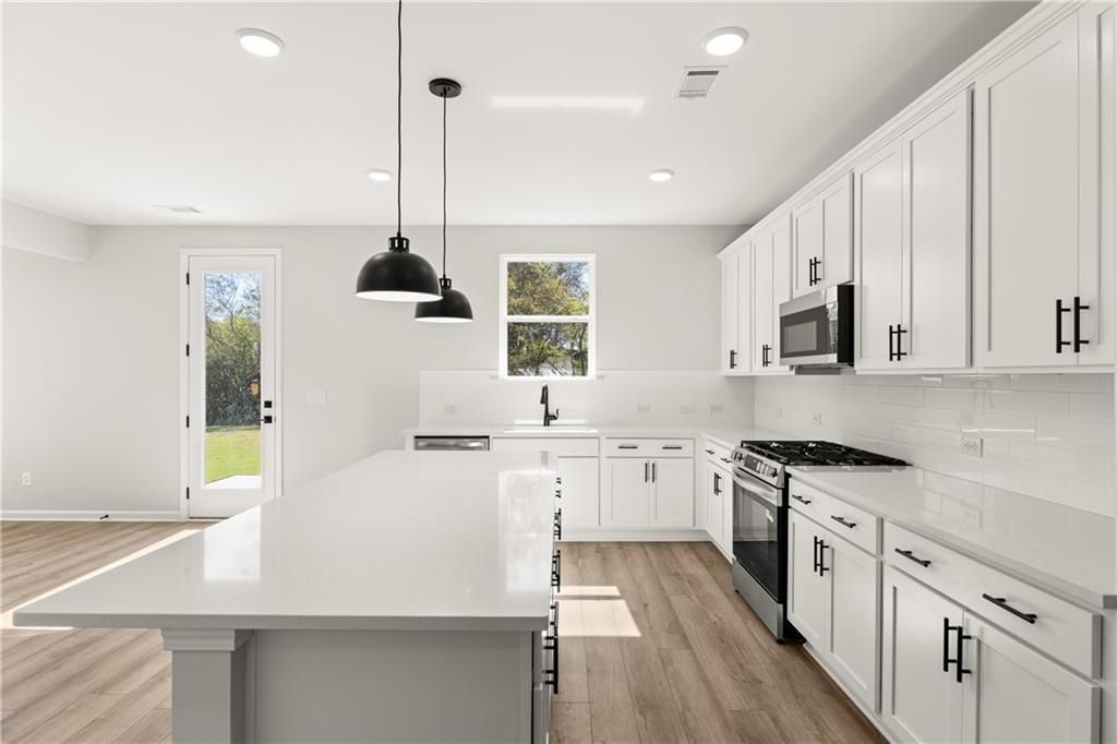 Modern white shaker kitchen with quartz island, stainless steel appliances, and backyard view in The Hickory B, Winder, GA