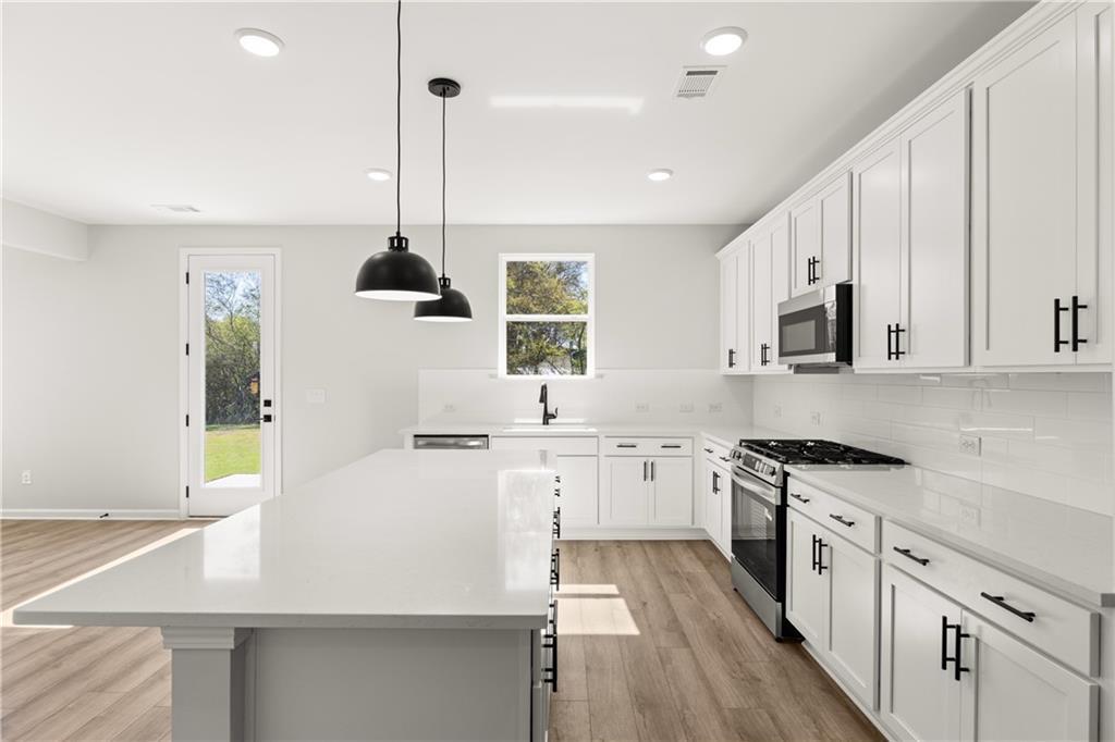 Modern white shaker kitchen with quartz island, stainless steel appliances, and backyard view in The Hickory B, Winder, GA