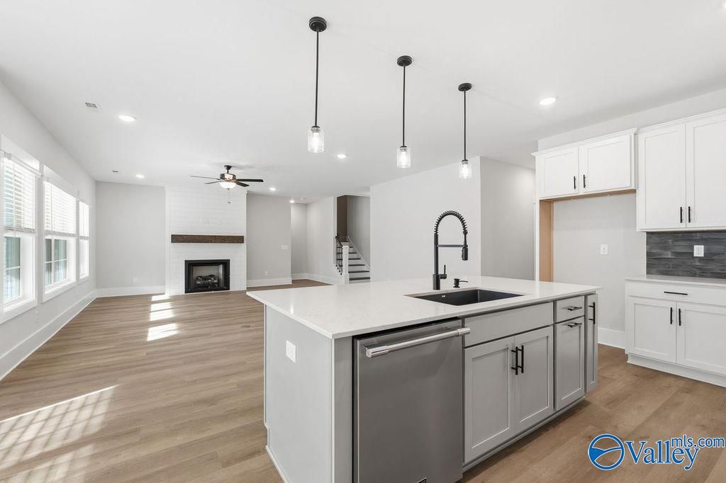 Modern open-concept kitchen with white quartz island, farmhouse sink, and living area fireplace in Davidson Homes The Rockford, Hartselle, Alabama