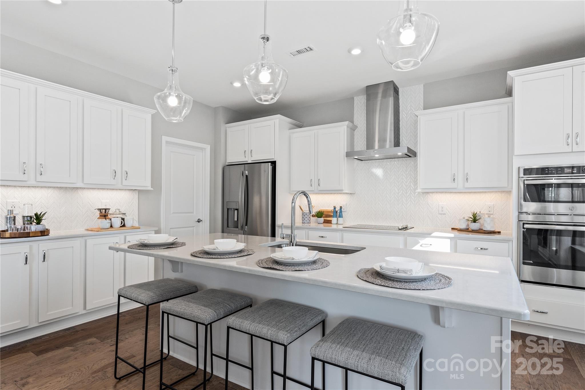 Bright kitchen with white cabinets, large island, stainless steel appliances, pendant lights in Davidson Homes The Hemlock A, Belmont, NC