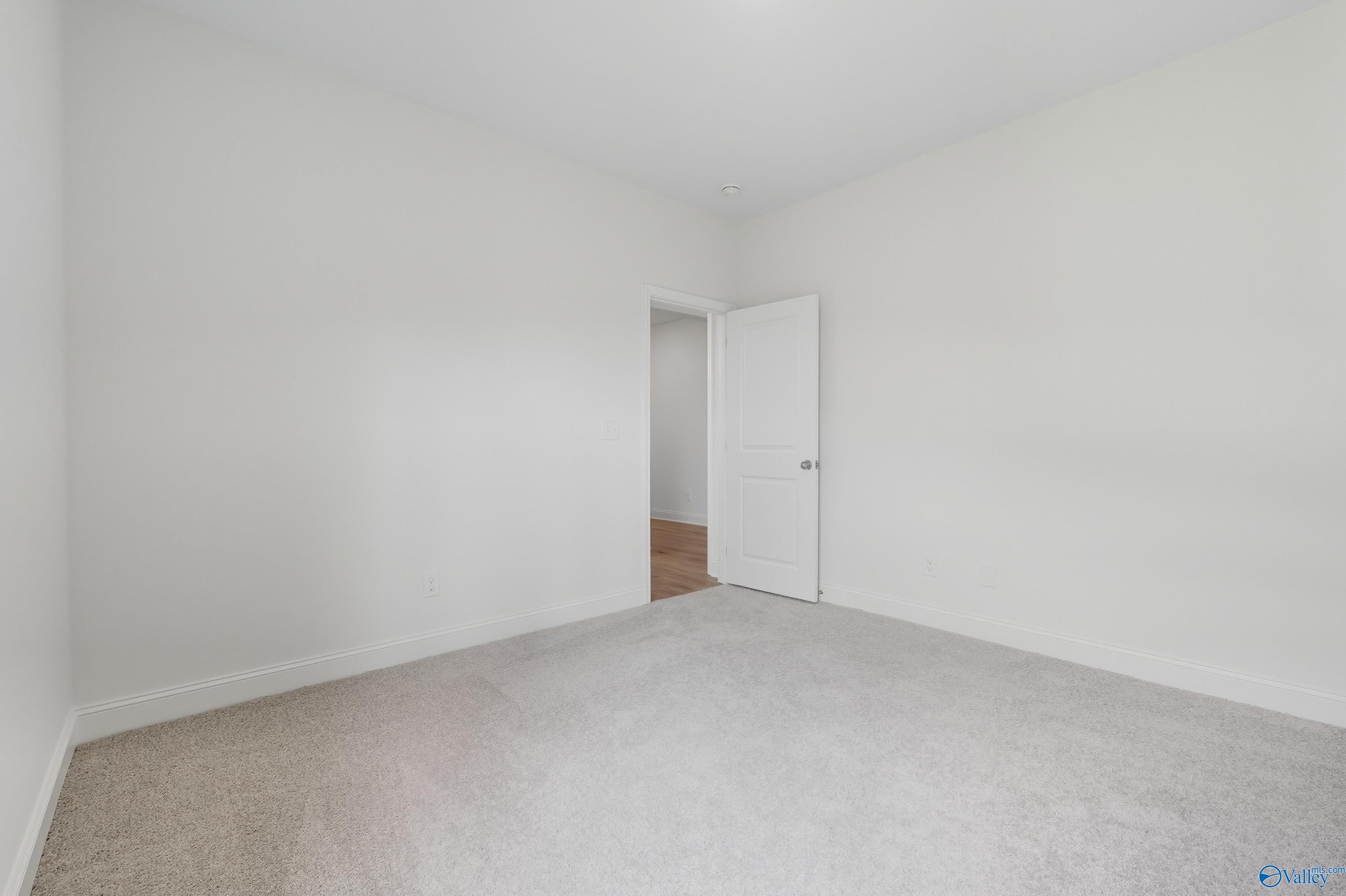 Bright empty secondary bedroom with white walls, beige carpet, and open door in Davidson Homes The Everett, Meridianville, Alabama
