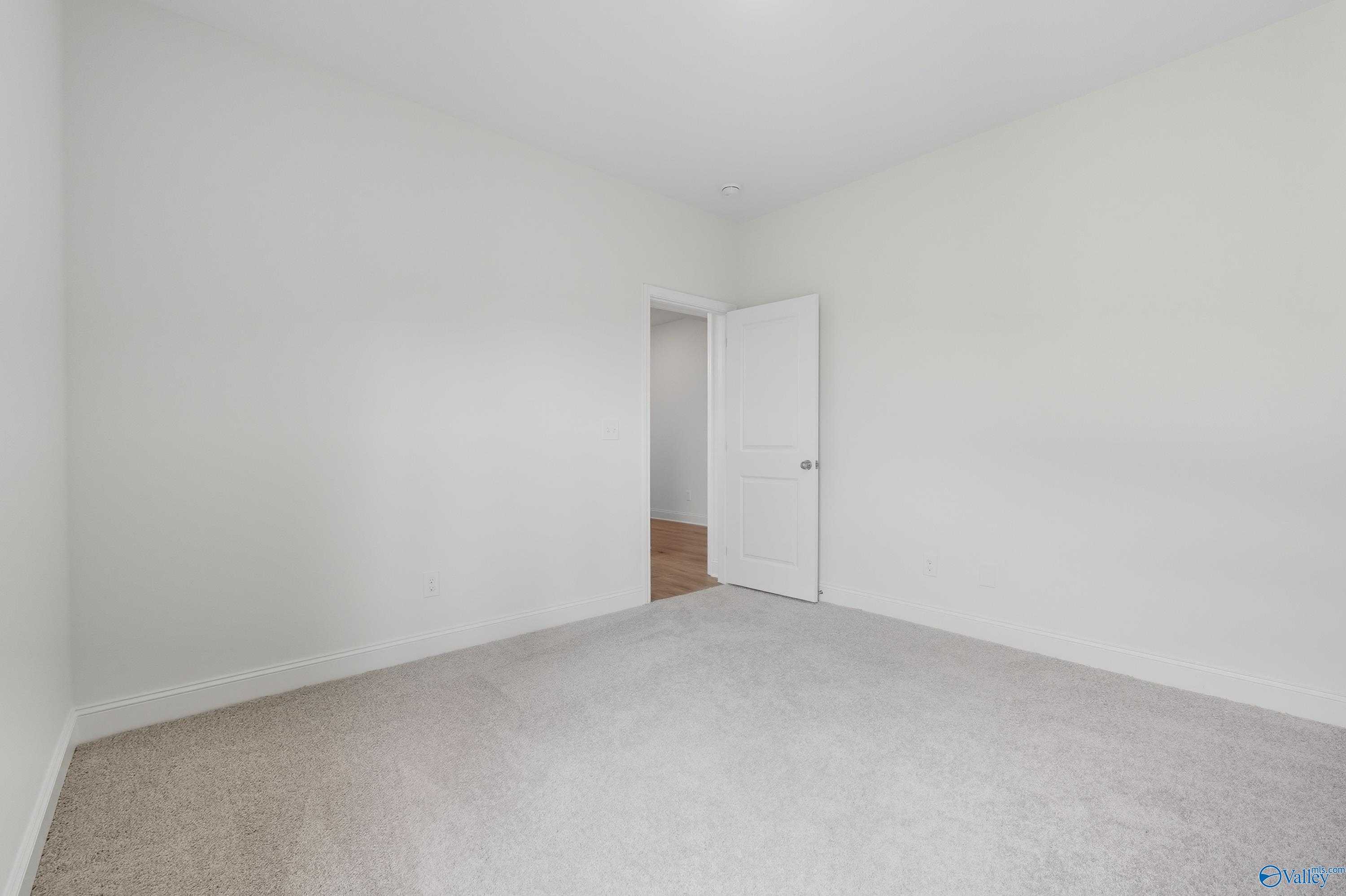 Empty bedroom with white walls, beige carpet, and open door to adjacent room in The Everett 4-bedroom home, Meridianville, Alabama
