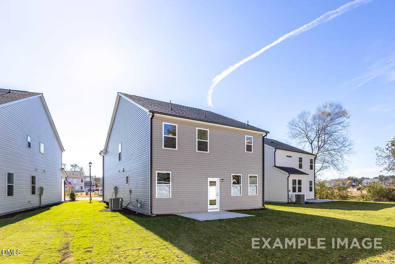 Rear view of two-story Adalynn A home featuring covered patio, lush green lawn, and backyard in Gregory Village, Lillington, NC