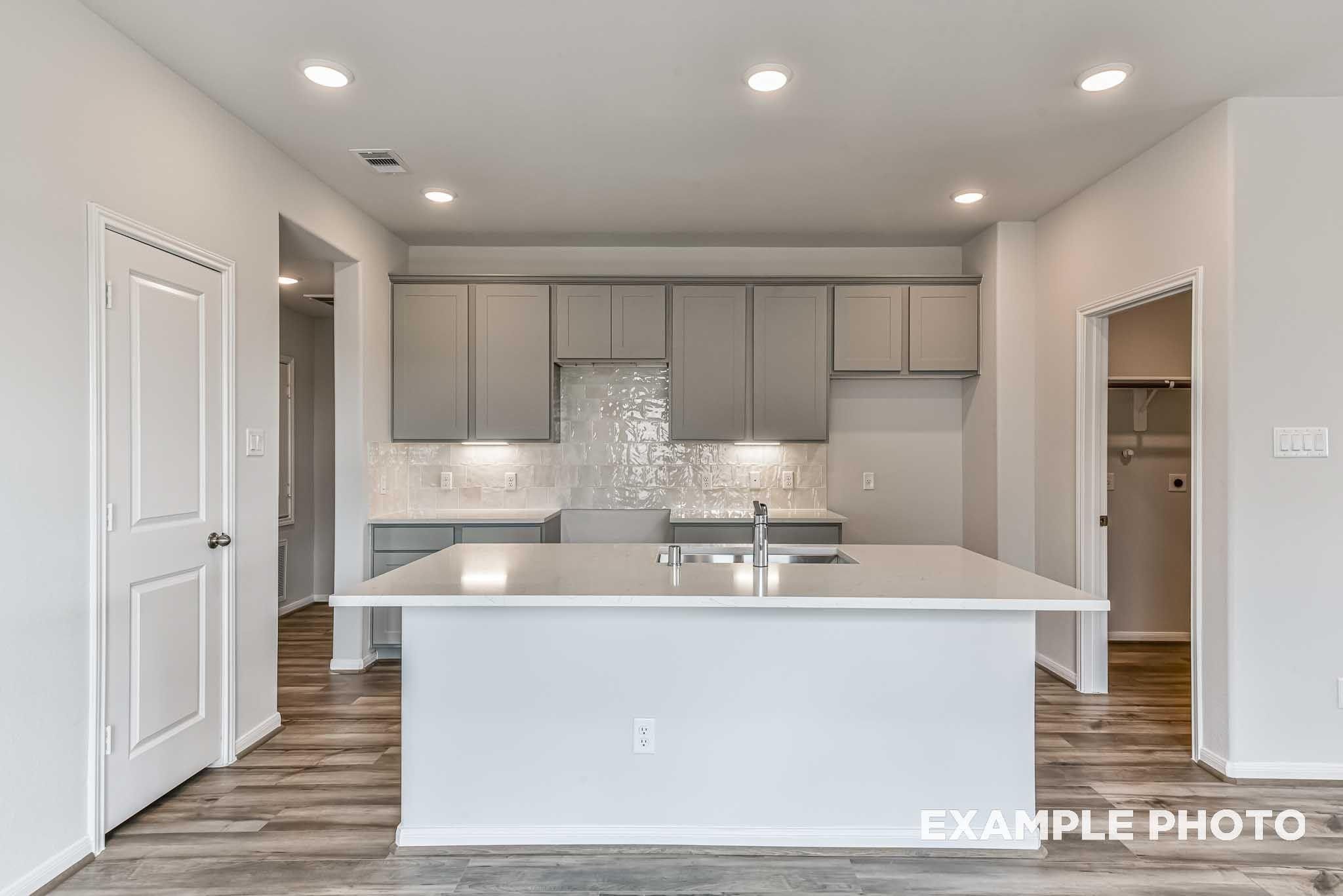 Modern kitchen with white island, gray shaker cabinets, subway tile backsplash, and wood-look flooring in Davidson Homes Costa A plan
