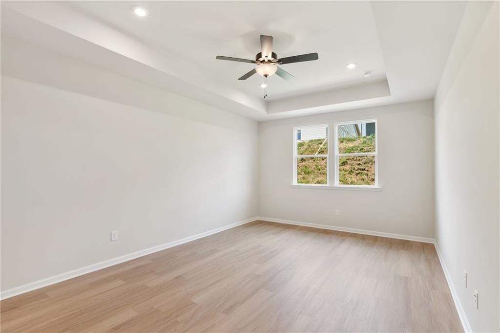 Bright empty bedroom with ceiling fan, hardwood floors, and large windows overlooking greenery in Davidson Homes The Daphne C, Loganville, GA