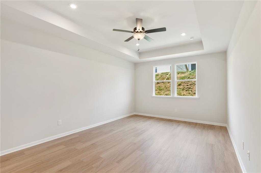 Spacious bedroom with hardwood floors, tray ceiling fan, recessed lights, and large windows in Davidson Homes The Daphne C, Loganville, GA