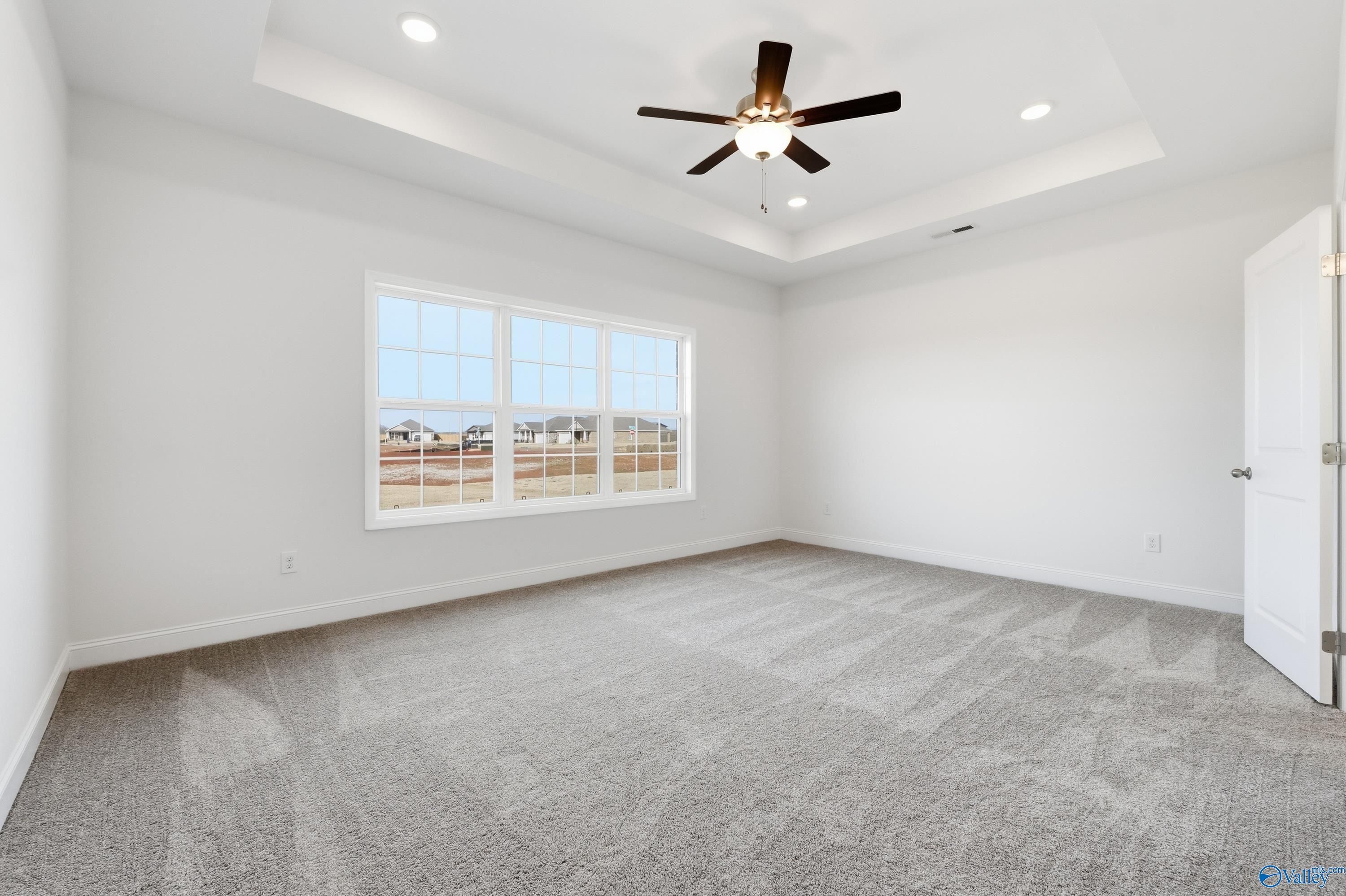 Bright bedroom with tray ceiling, ceiling fan, large window overlooking neighborhood in Davidson Homes The Montgomery C, Harvest, AL