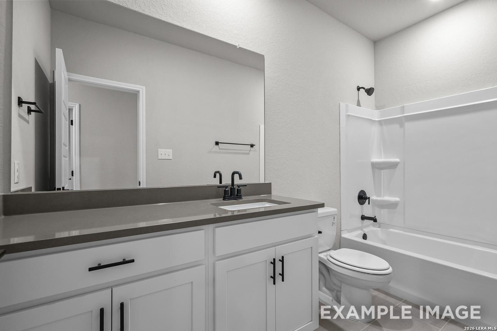 Modern bathroom with white vanity, dark hardware, and shower-tub combo in The Glenwood E by Davidson Homes, San Antonio.