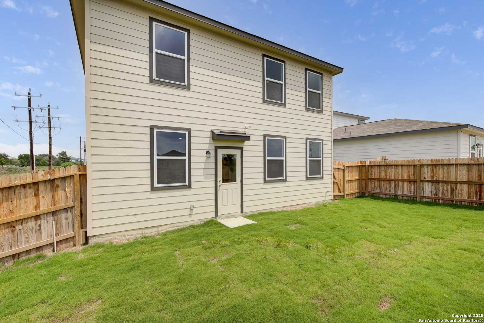 Two-story beige home with side entrance, large windows, fenced grassy backyard in Applewhite Meadows, San Antonio
