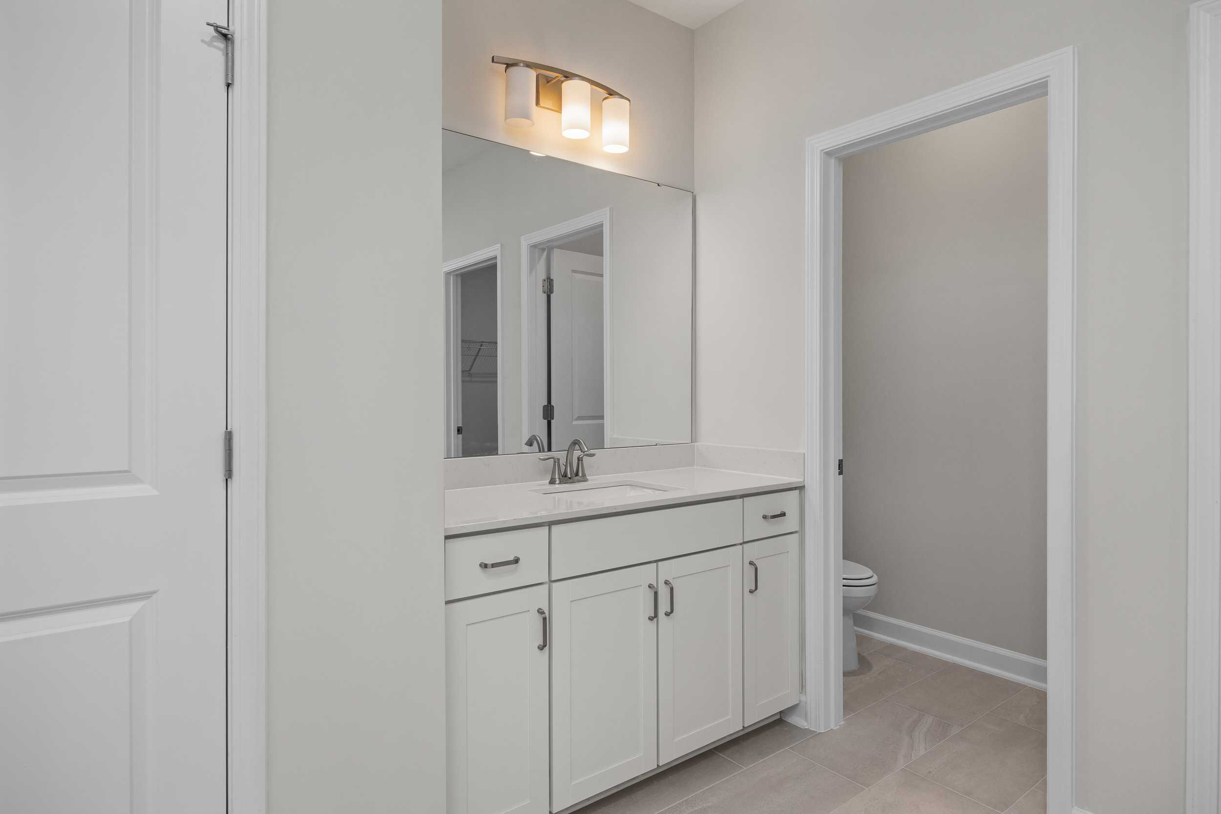 The Aspen master bathroom featuring white double vanity, large mirror, wall sconce lighting, and walk-in shower door