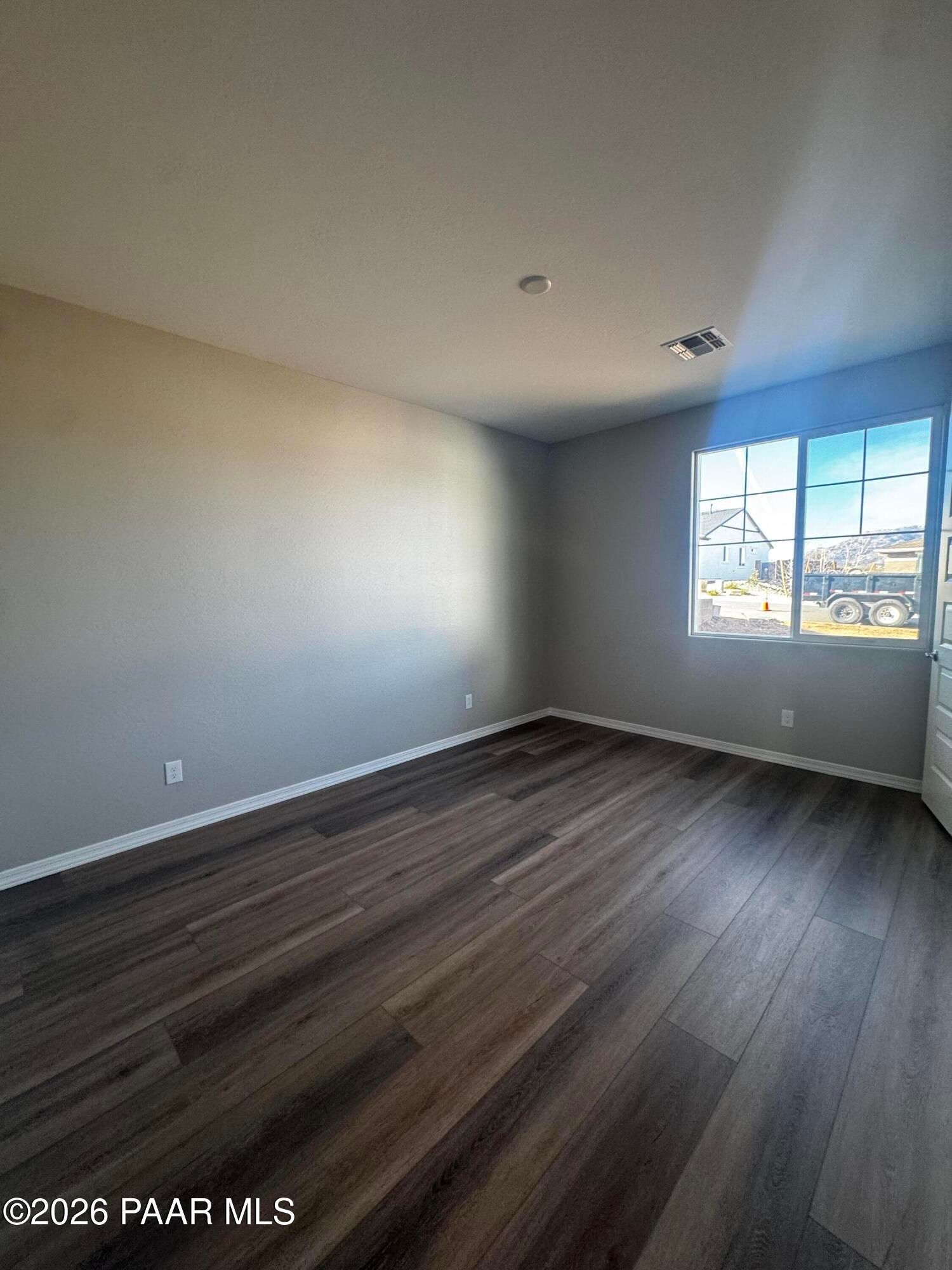 Empty bedroom with light gray walls, luxury vinyl plank floors, and large window overlooking construction in Davidson Homes Daybreak B, Prescott AZ