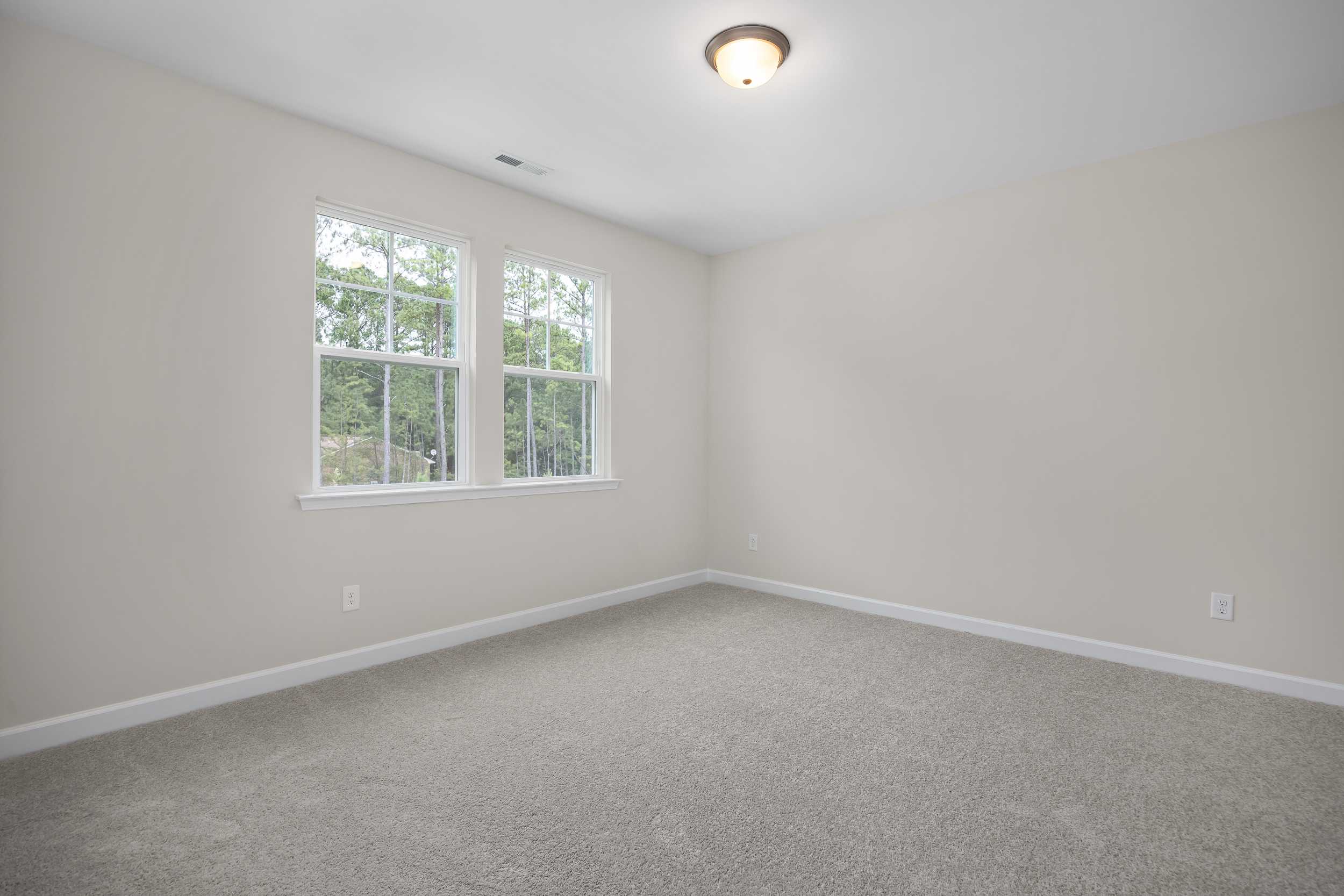Spacious empty bedroom in The Beech C with beige walls, large double windows overlooking trees, carpeted floor, ceiling light