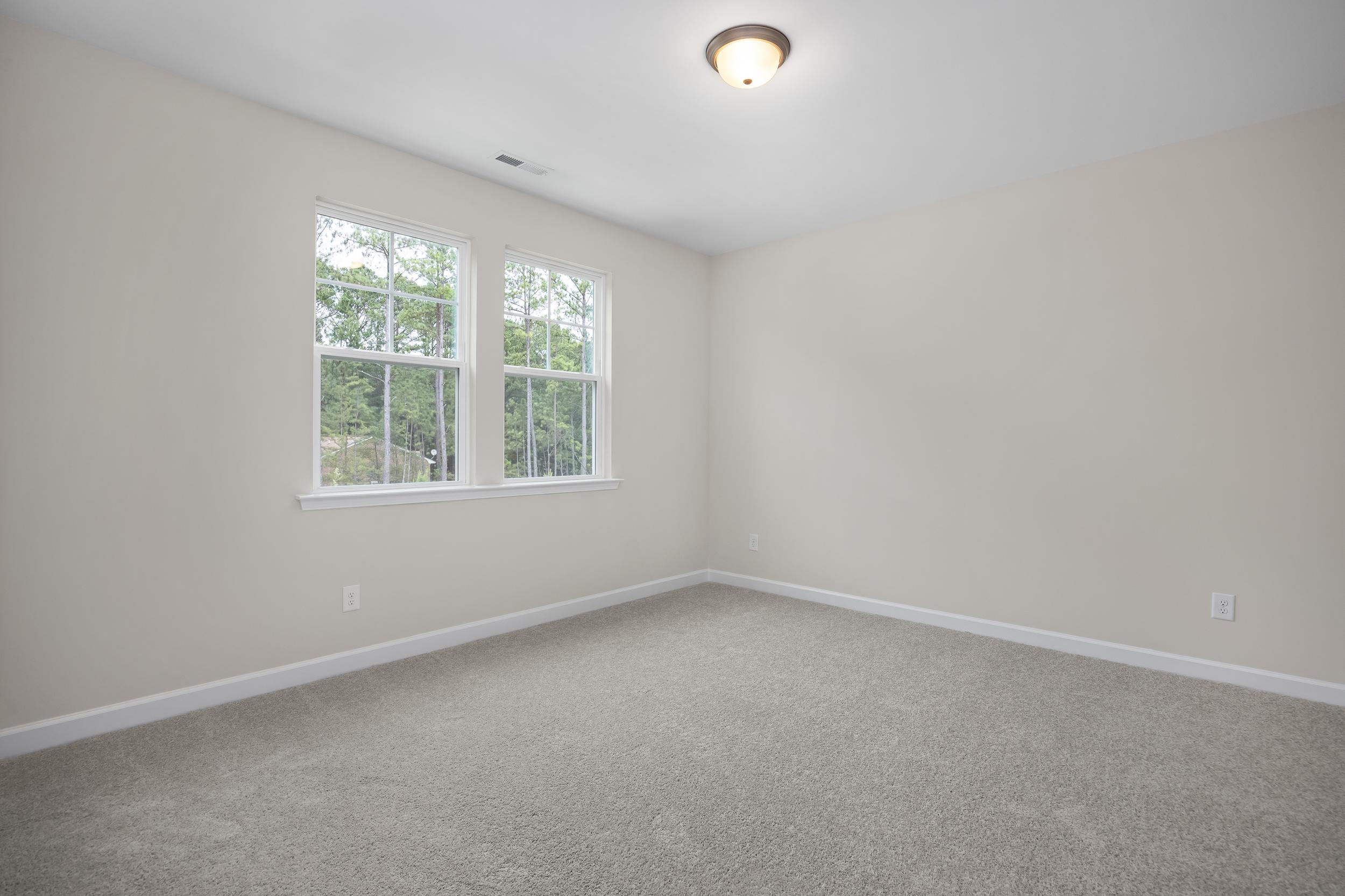 Spacious upstairs bedroom in The Beech A with beige walls, large double windows overlooking trees, and carpeted floor