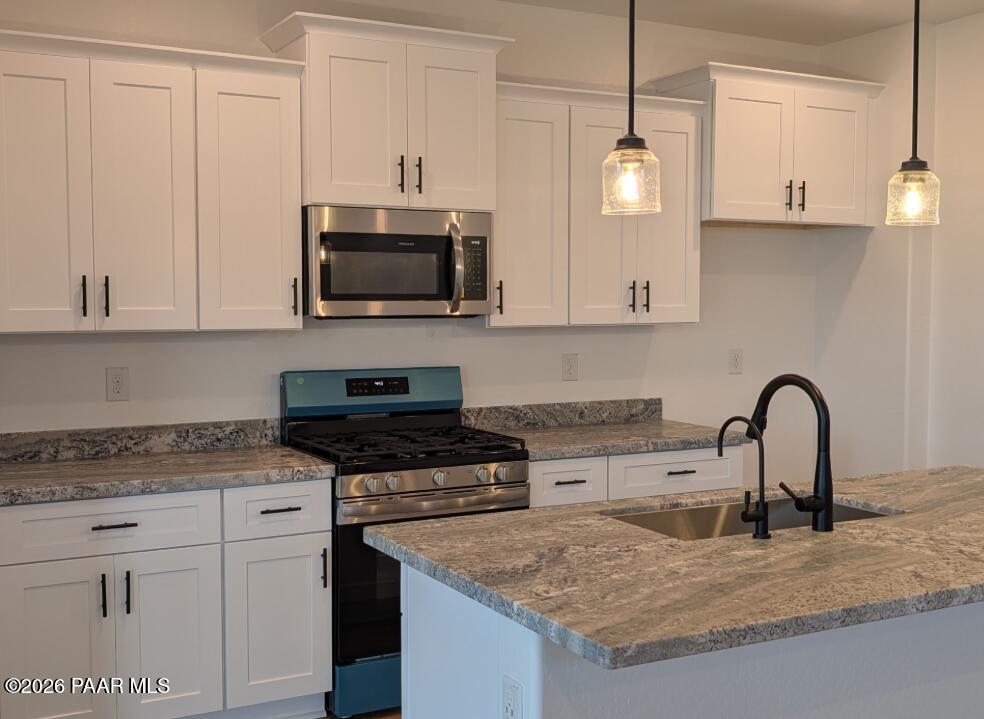 White shaker kitchen with granite island, stainless gas range, and pendant lights in Davidson Homes The Newport A, Prescott