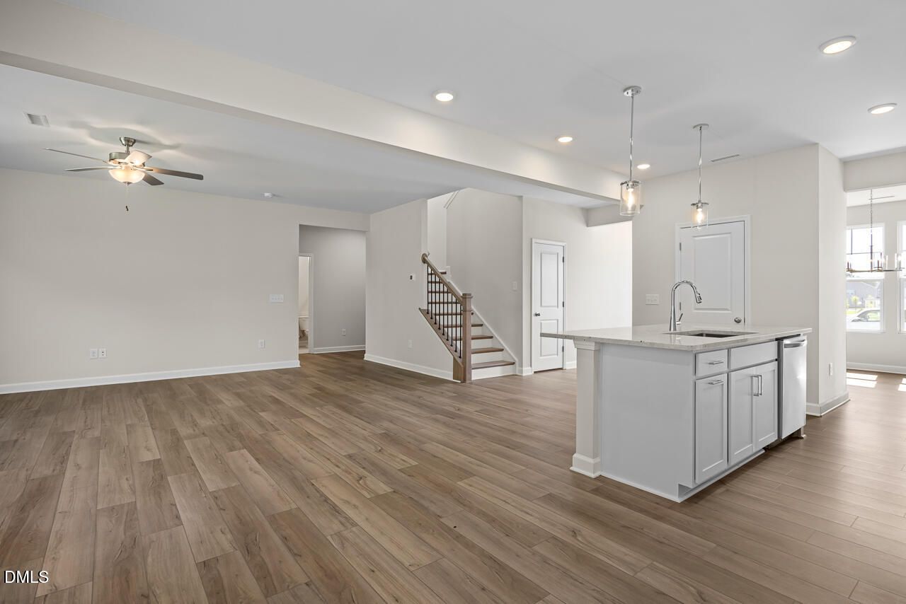 Open-concept living area with luxury vinyl plank flooring, white kitchen island, and staircase in Davidson Homes Willow C, Zebulon NC