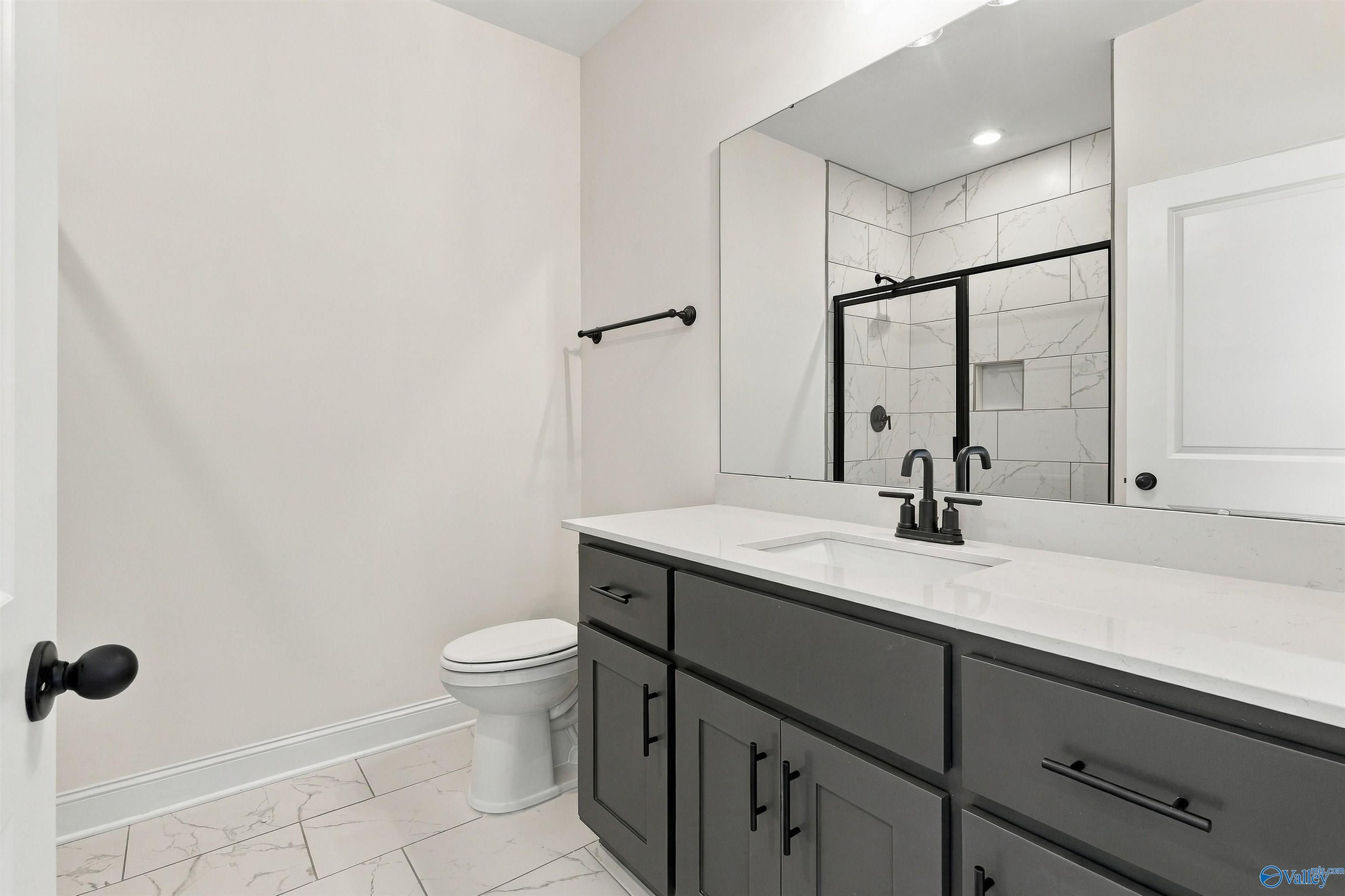 Modern bathroom with gray vanity, quartz countertop, matte black fixtures, and tiled walk-in shower in Huntsville, Alabama new home