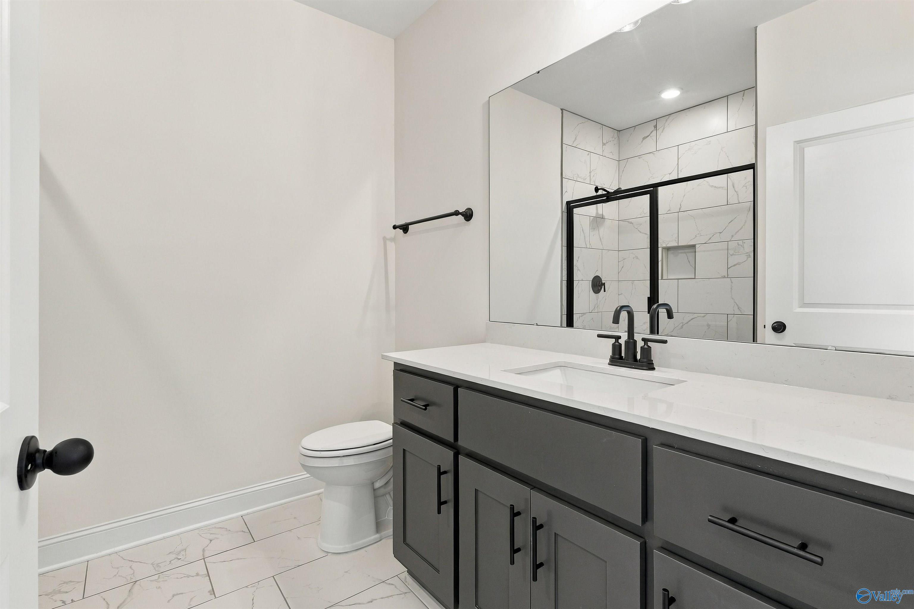 Modern bathroom with gray vanity, quartz countertop, matte black fixtures, and tiled walk-in shower in Huntsville, Alabama new home