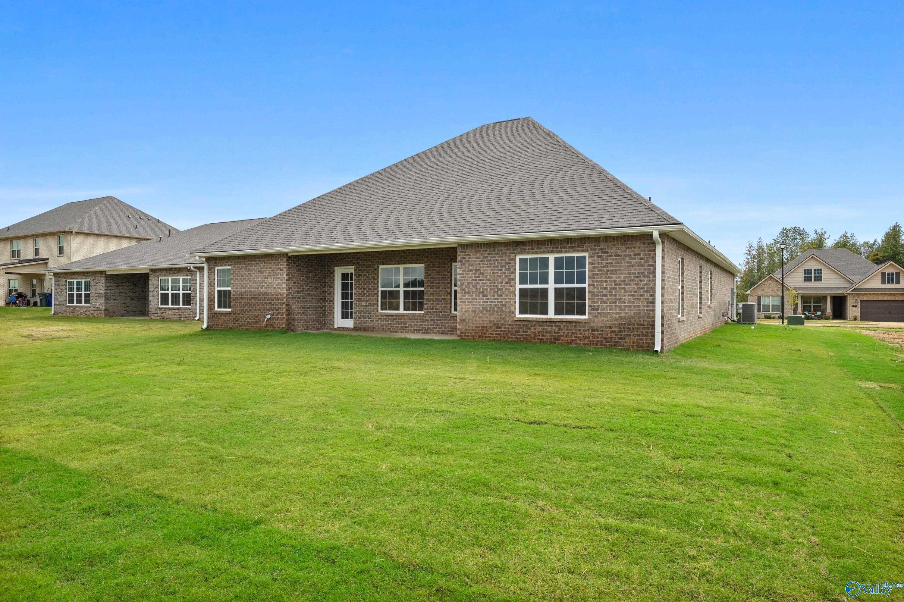 Rear view of brick 4-bedroom The Lanier home with gabled roof, French doors, and lush green backyard in Creekside, Harvest, Alabama