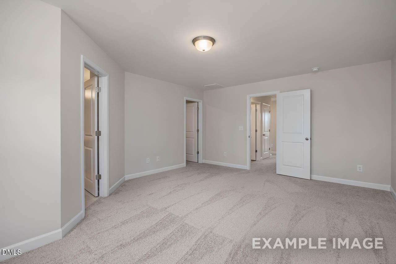 Spacious upstairs hallway with open doors to bedrooms, beige carpet, and neutral walls in Davidson Homes The Graham, Fuquay-Varina, NC