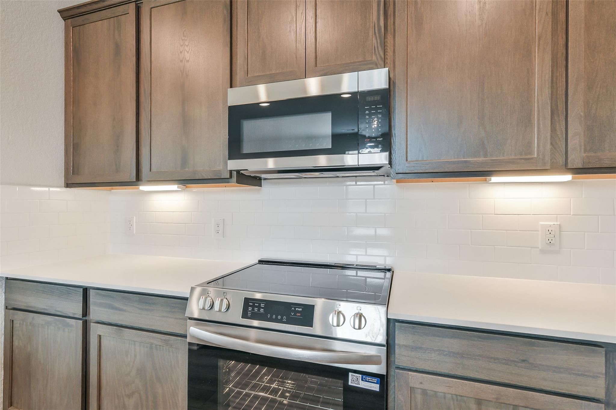 Modern kitchen with stainless steel range, microwave, subway tile backsplash, and wood cabinets in Davidson Homes The Brazos E, Cleveland, Texas