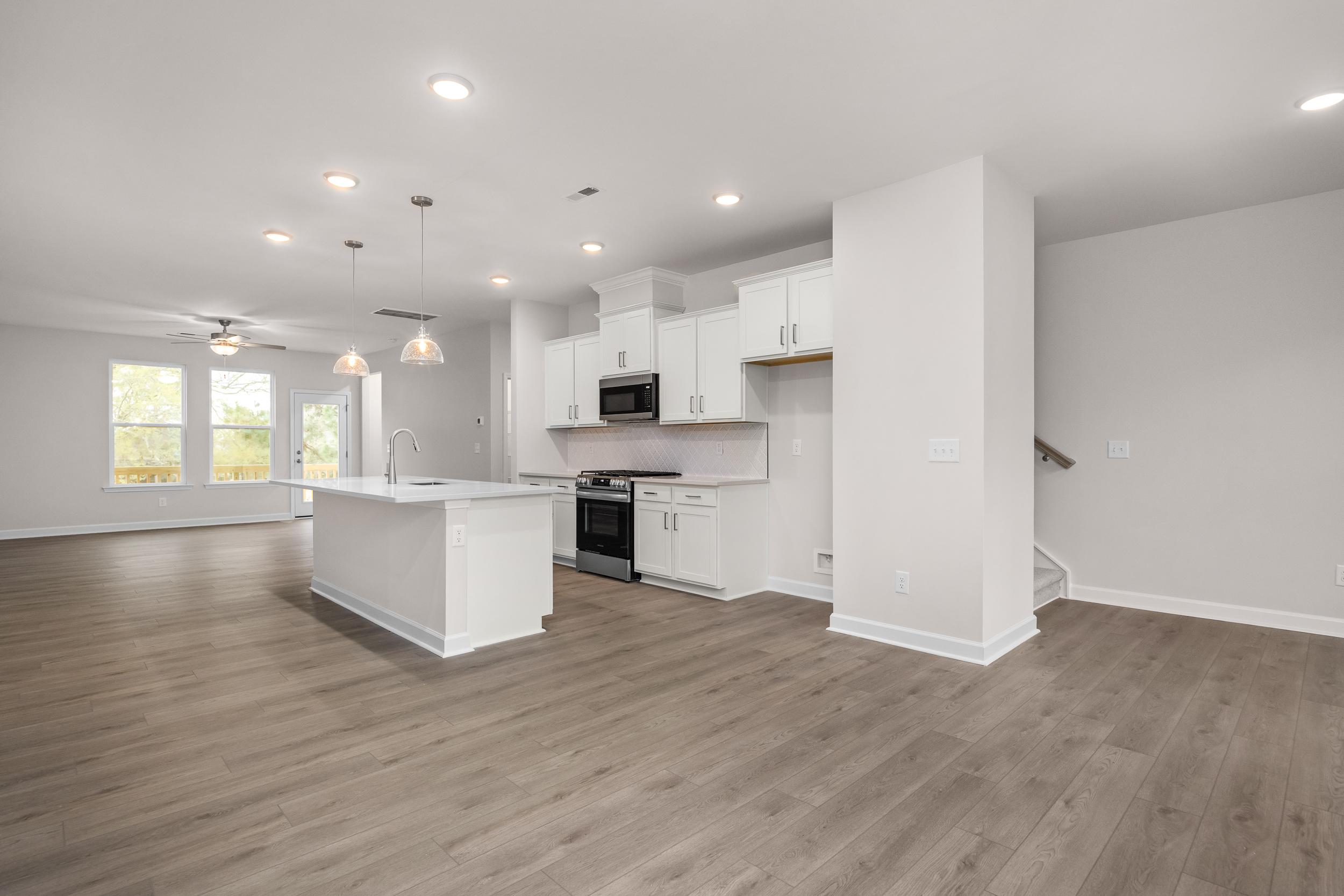 Spacious open-concept kitchen at Forestville Yard Townhomes in Knightdale NC with white cabinets, center island, stainless appliances, and hardwood floors