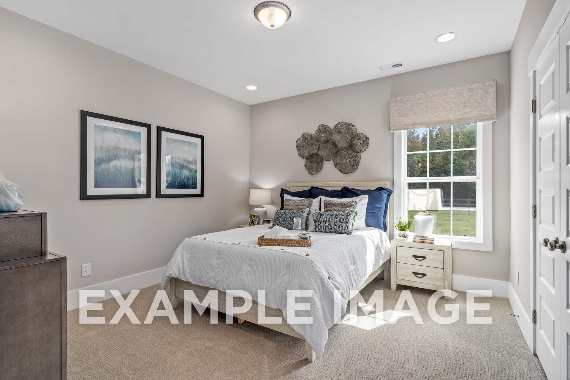 Spacious master bedroom in The Harrison B with white bed, blue accents, large window, and neutral walls