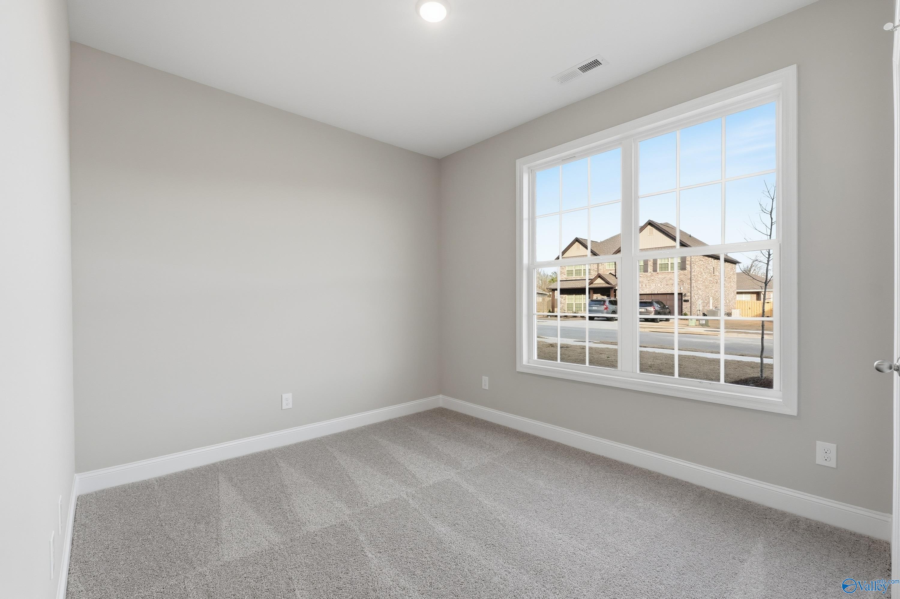Cozy bedroom with light gray walls, large window overlooking neighborhood in Davidson Homes The Asheville, Arab, Alabama