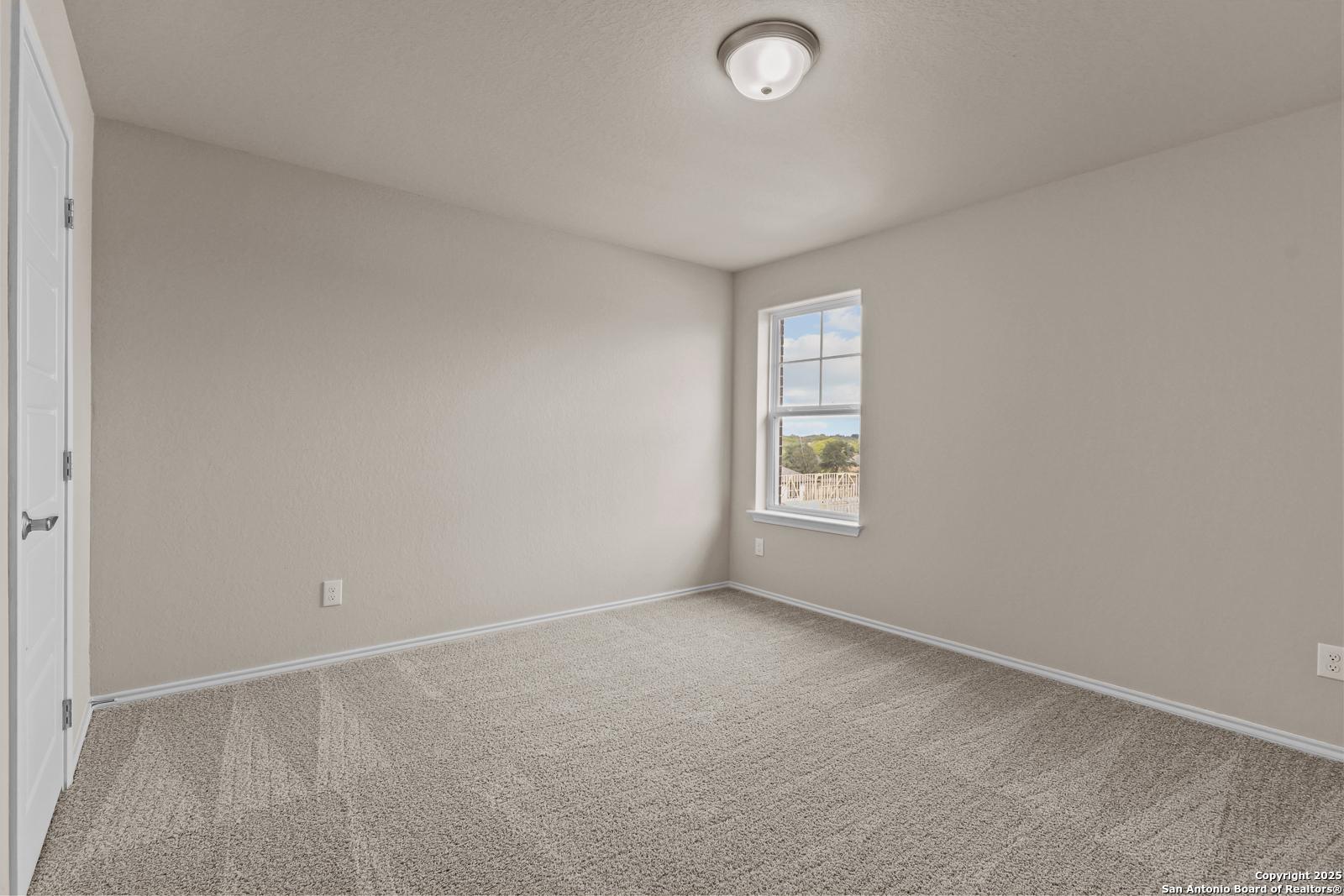 Bright secondary bedroom with beige walls, carpeted floor, and large window in 4-bedroom Davidson Homes The Douglas G, San Antonio
