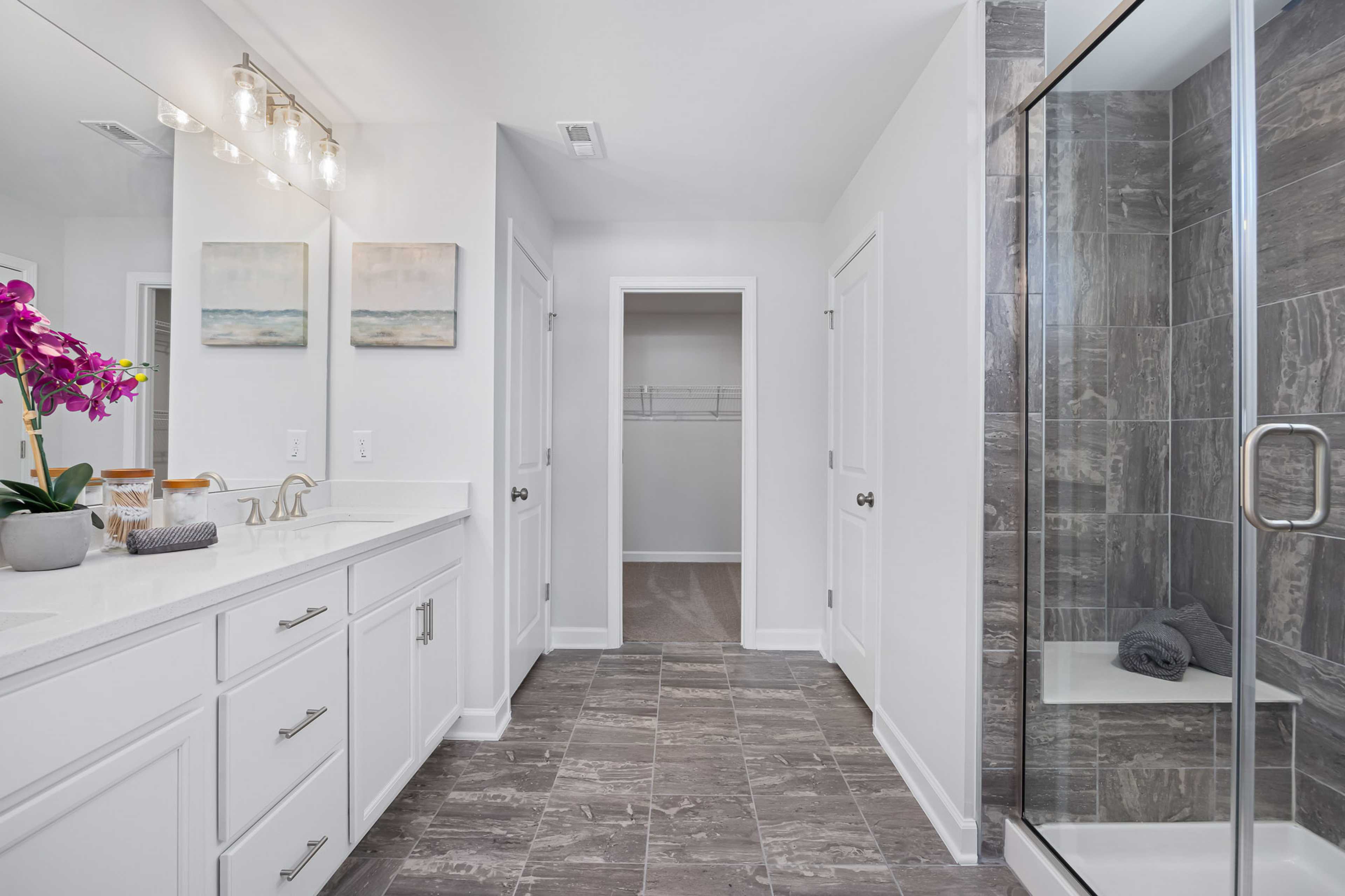 Spacious primary bathroom with white double vanity, frameless glass shower, and walk-in closet at Stagecoach Corner in Mebane, NC
