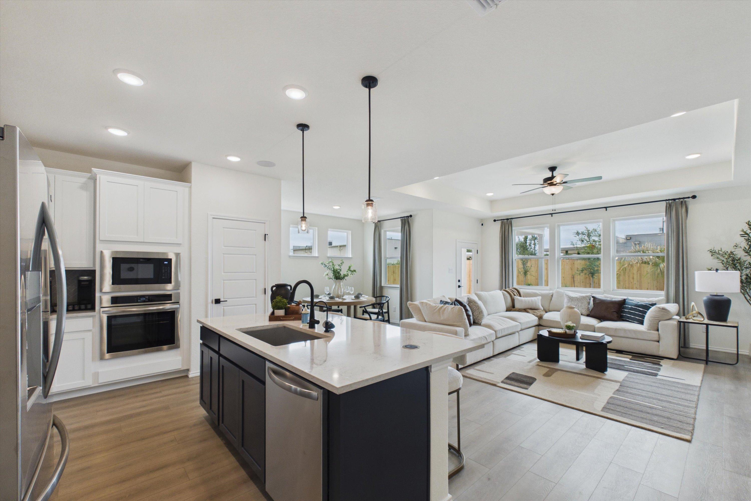 Open-concept kitchen living room in Rayburn Valley San Antonio TX by Davidson Homes with white cabinets quartz island sectional sofa and hardwood floors