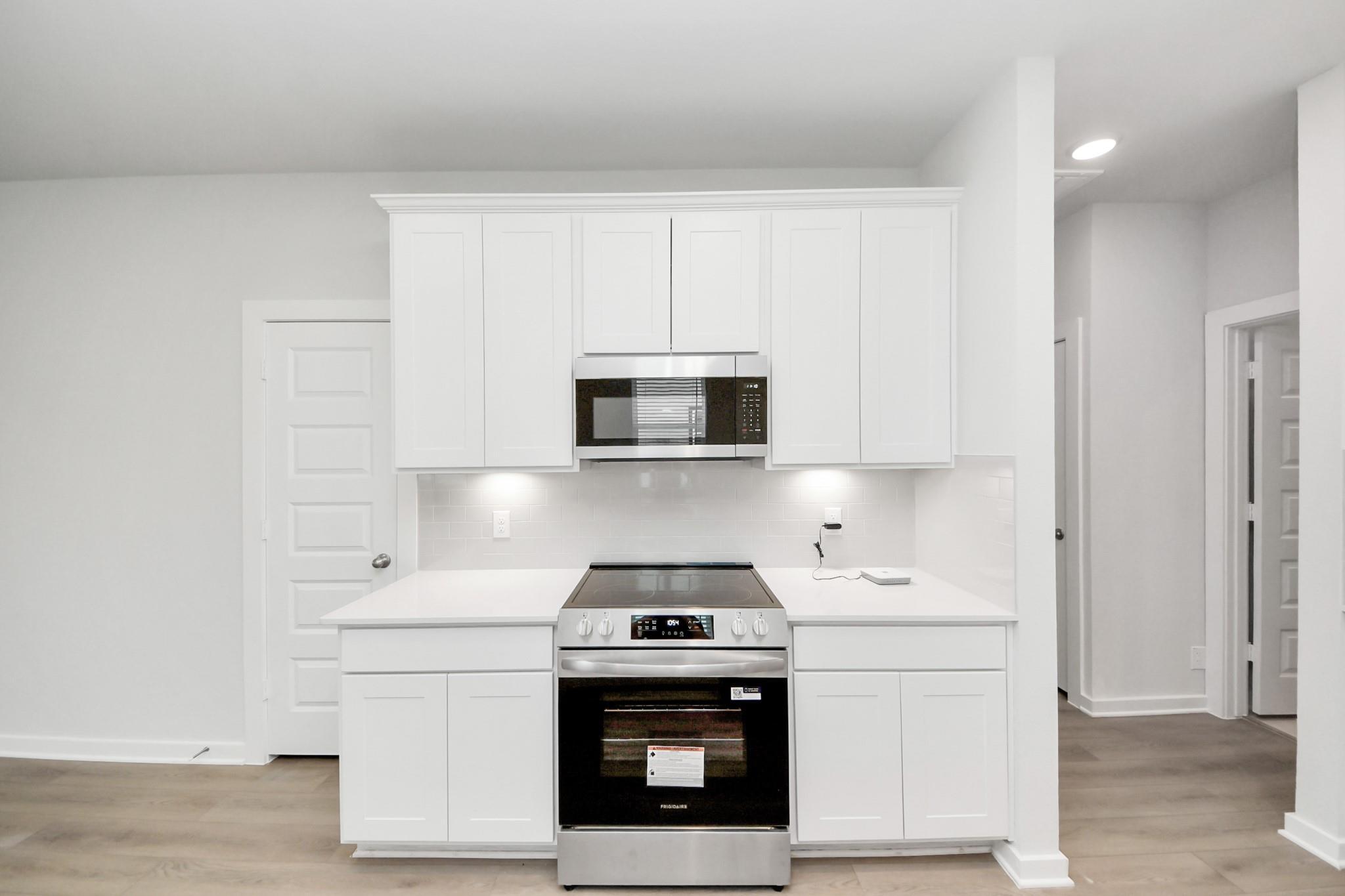 Modern kitchen with white cabinets, stainless steel appliances, and quartz countertops in The Frio F plan, Cleveland, TX.