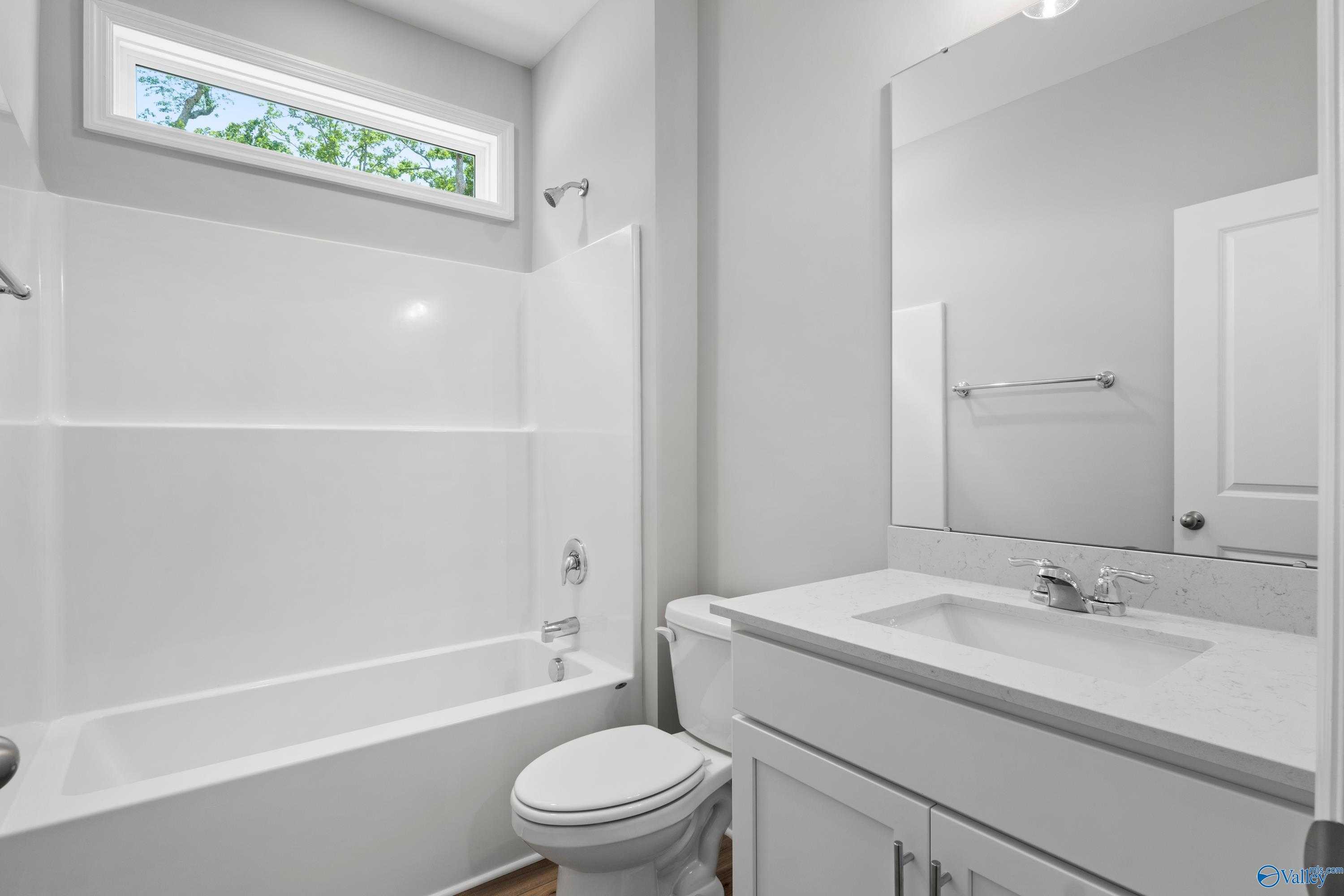 Modern bathroom with white tub-shower combo, vanity sink, large mirror, and clerestory window in Davidson Homes Chelsea B, New Market, Alabama