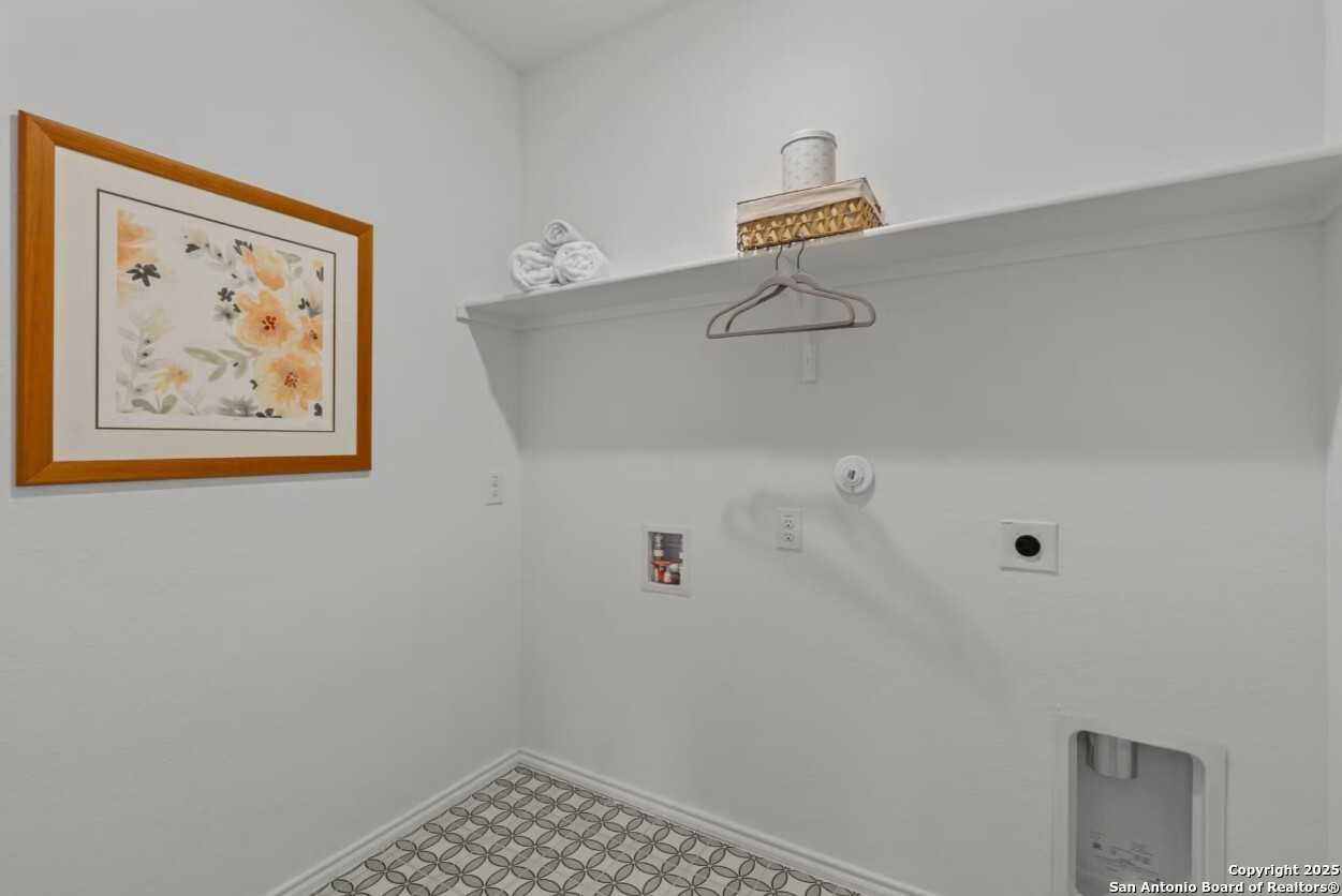Bright laundry room with utility sink, white shelves, floral framed art in 4-bedroom Davidson Homes Daphne J, Elmendorf, Texas