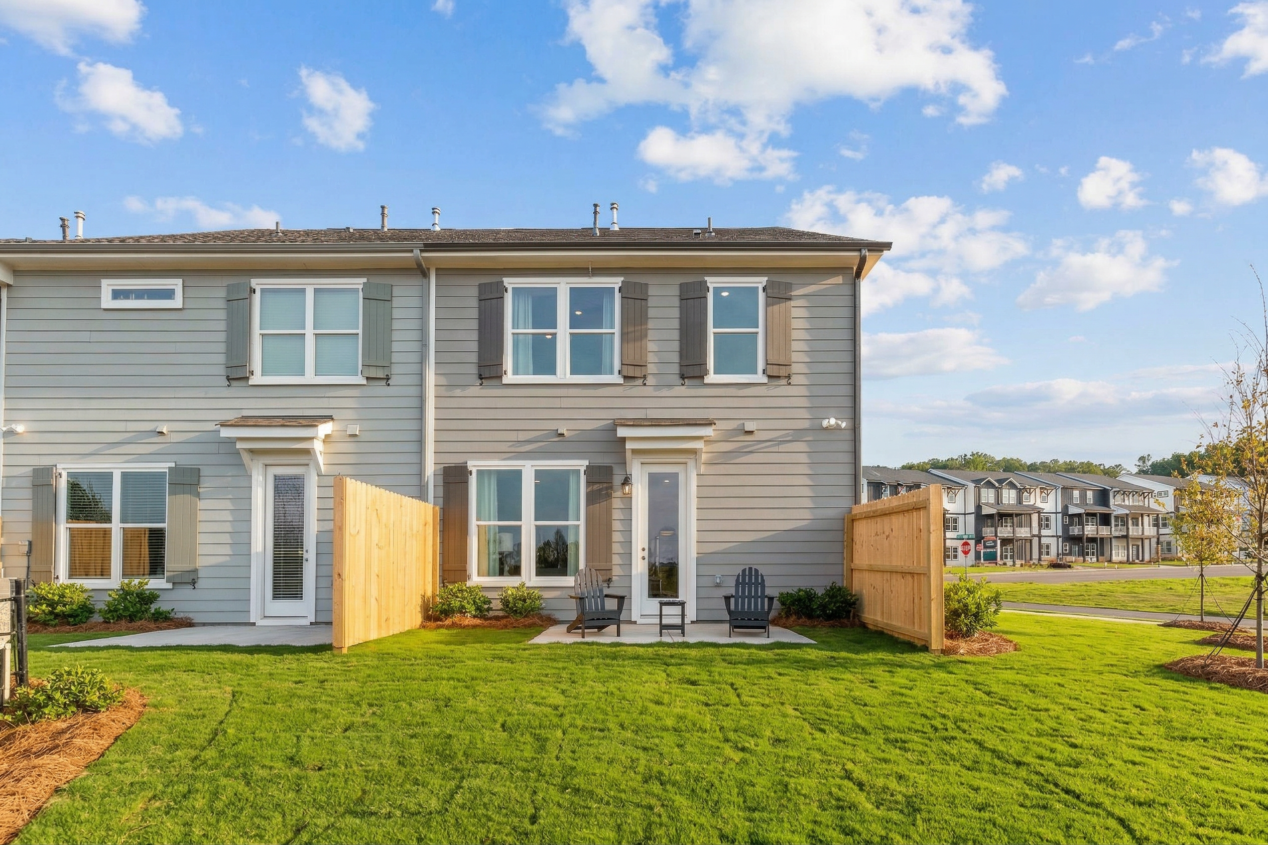 Modern gray townhomes with shutters, fenced backyards, patio chairs, and lush green lawns at Hemingway in Cumming, Georgia