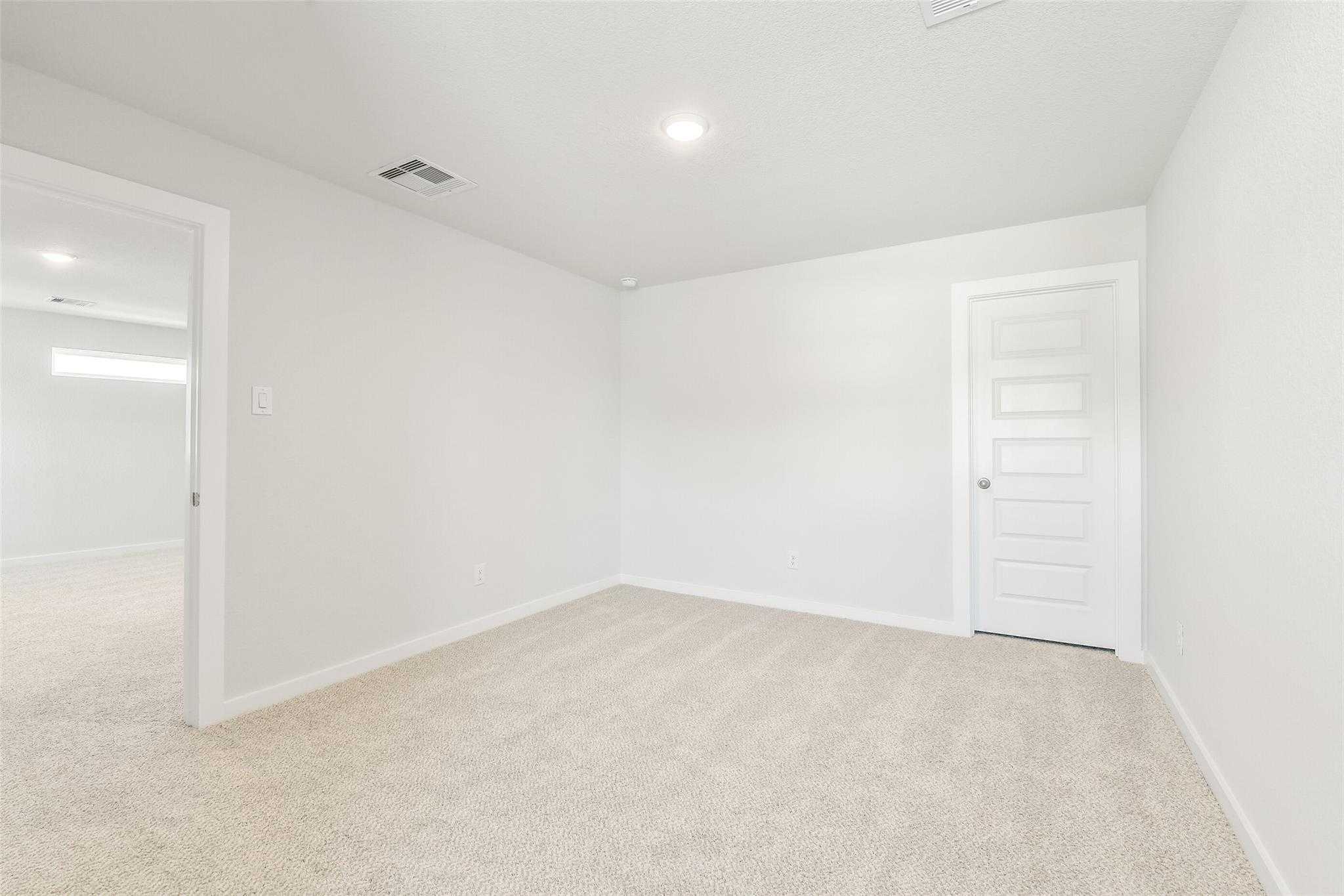 Spacious empty bedroom with beige carpet and white walls in Davidson Homes San Marcos E, Cleveland Texas