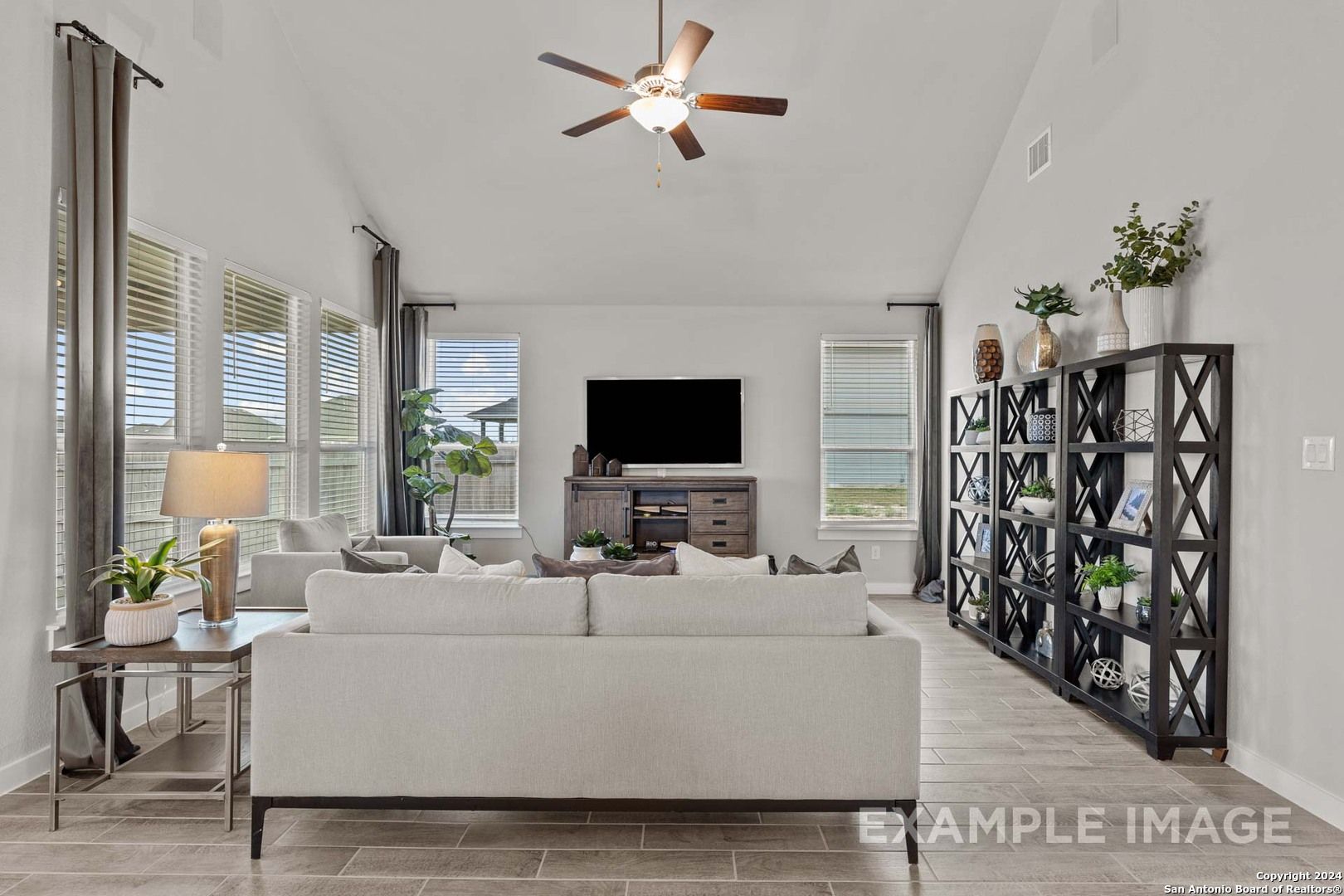 Bright open living room with high ceilings, ceiling fan, beige sofa, and large windows in Davidson Homes The Collin A, Seguin, Texas