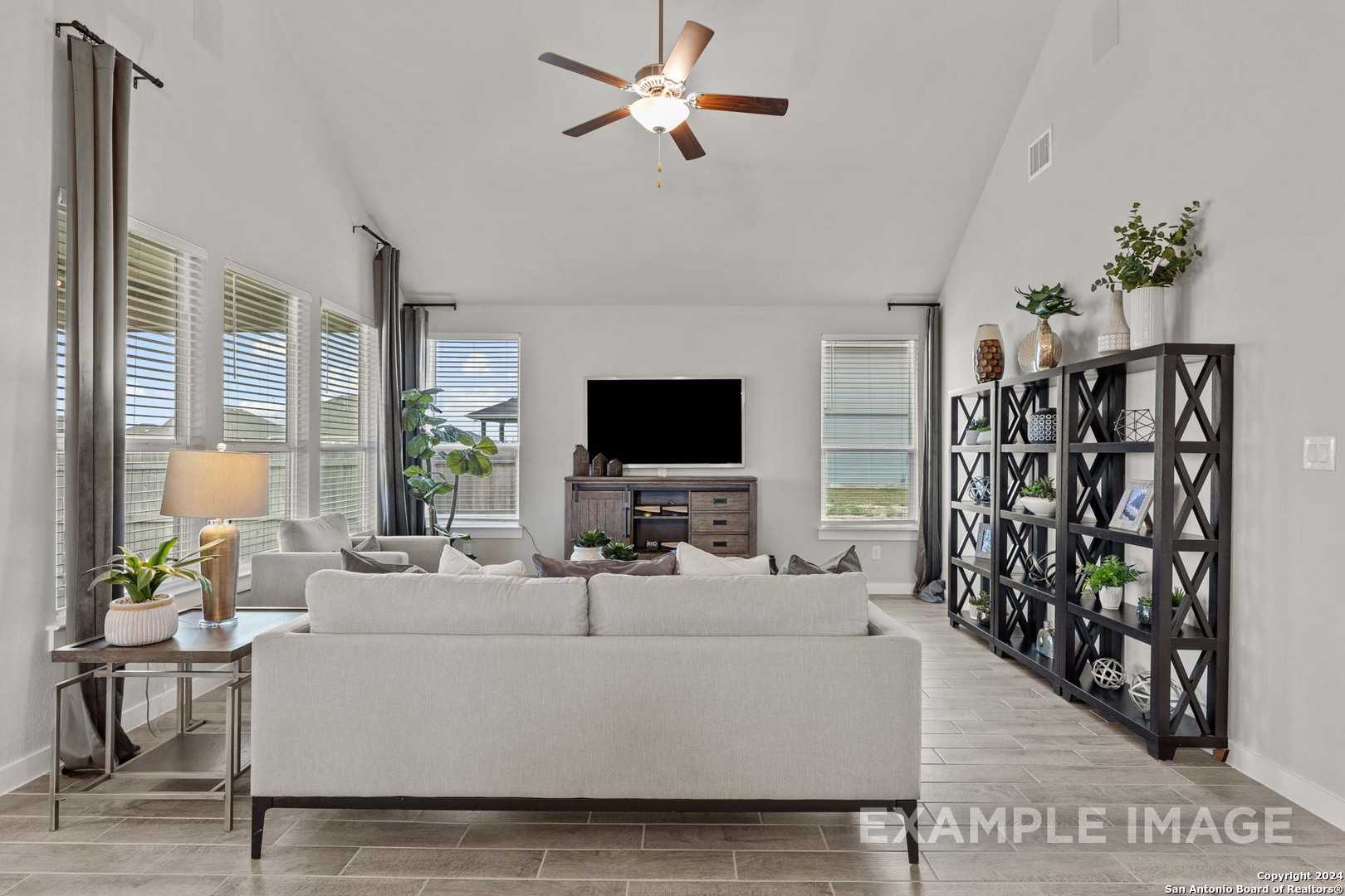 Bright open living room with high ceilings, ceiling fan, beige sofa, and large windows in Davidson Homes The Collin A, Seguin, Texas