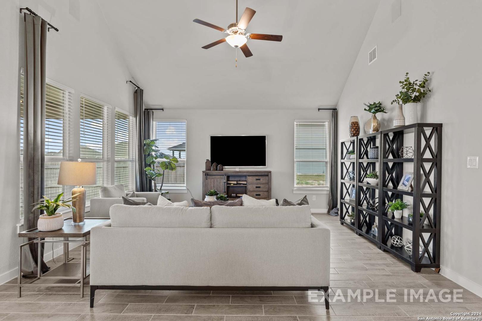 Bright open living room with high ceilings, ceiling fan, beige sofa, and large windows in Davidson Homes The Collin A, Seguin, Texas