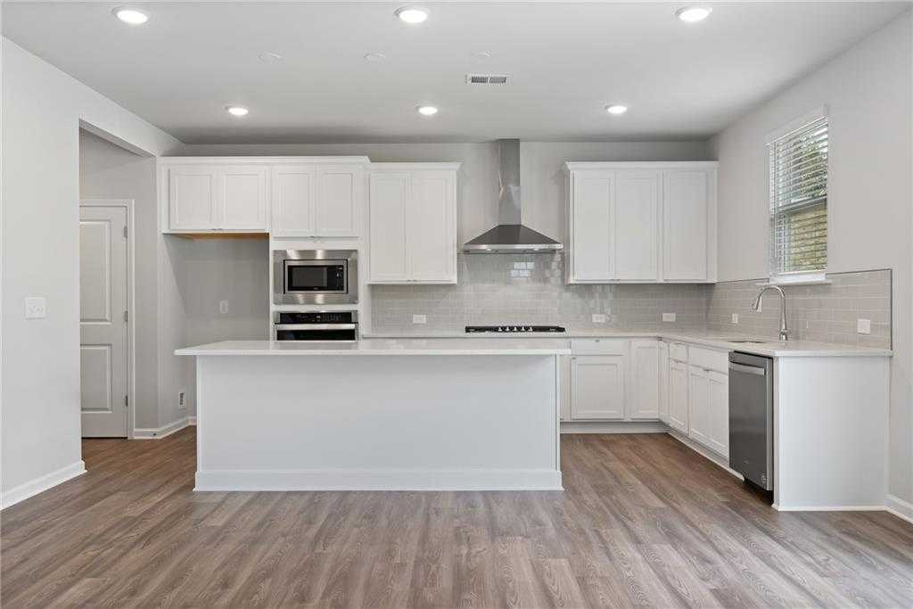 Modern white kitchen with large island, stainless steel appliances, and quartz counters in Davidson Homes The Hickory B, Winder, GA