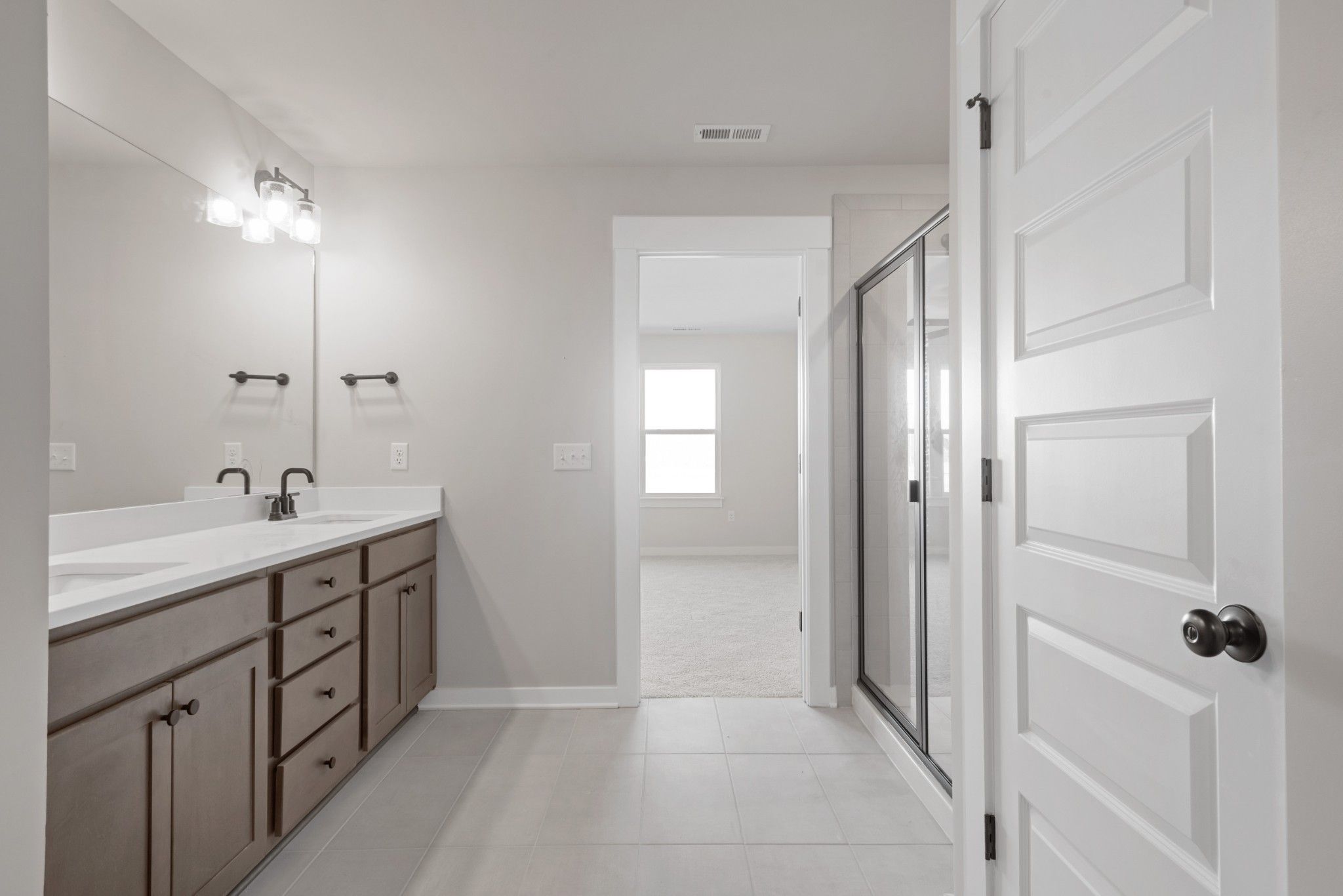 Modern master bathroom with double vanity, frameless glass shower, and adjacent bedroom in Davidson Homes The Willow B, Calista Farms